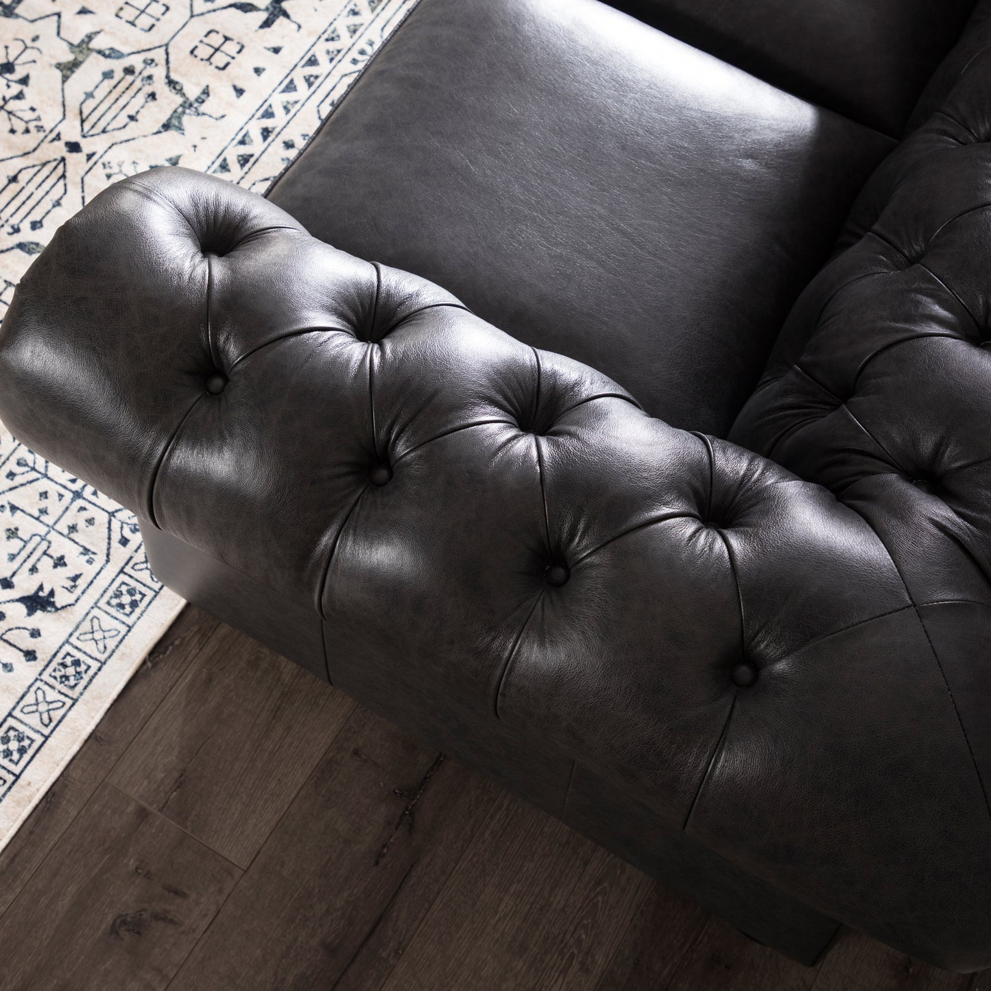 Dark gray tufted leather chesterfield sofa armrest on a patterned rug