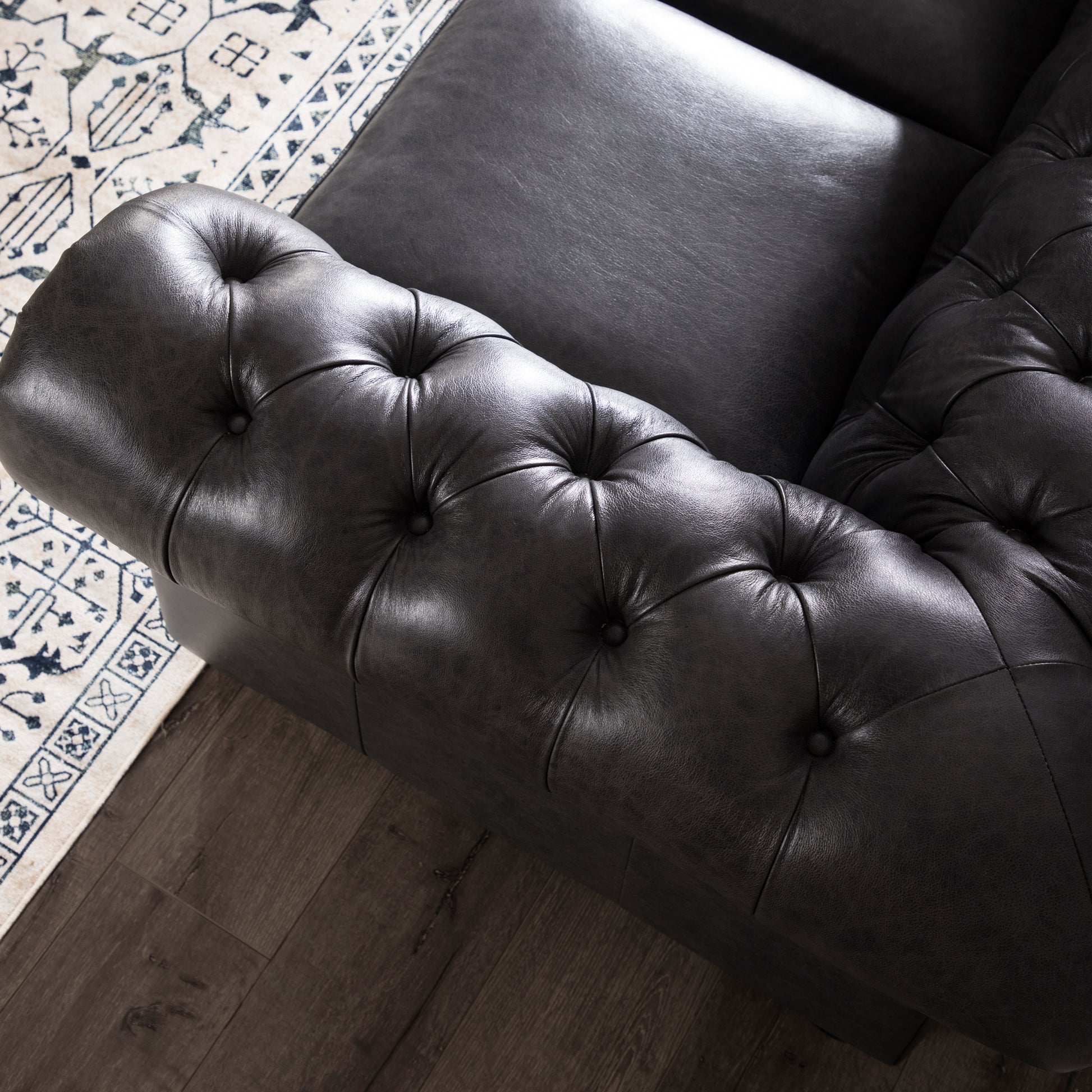 Dark gray tufted leather chesterfield sofa armrest on a patterned rug
