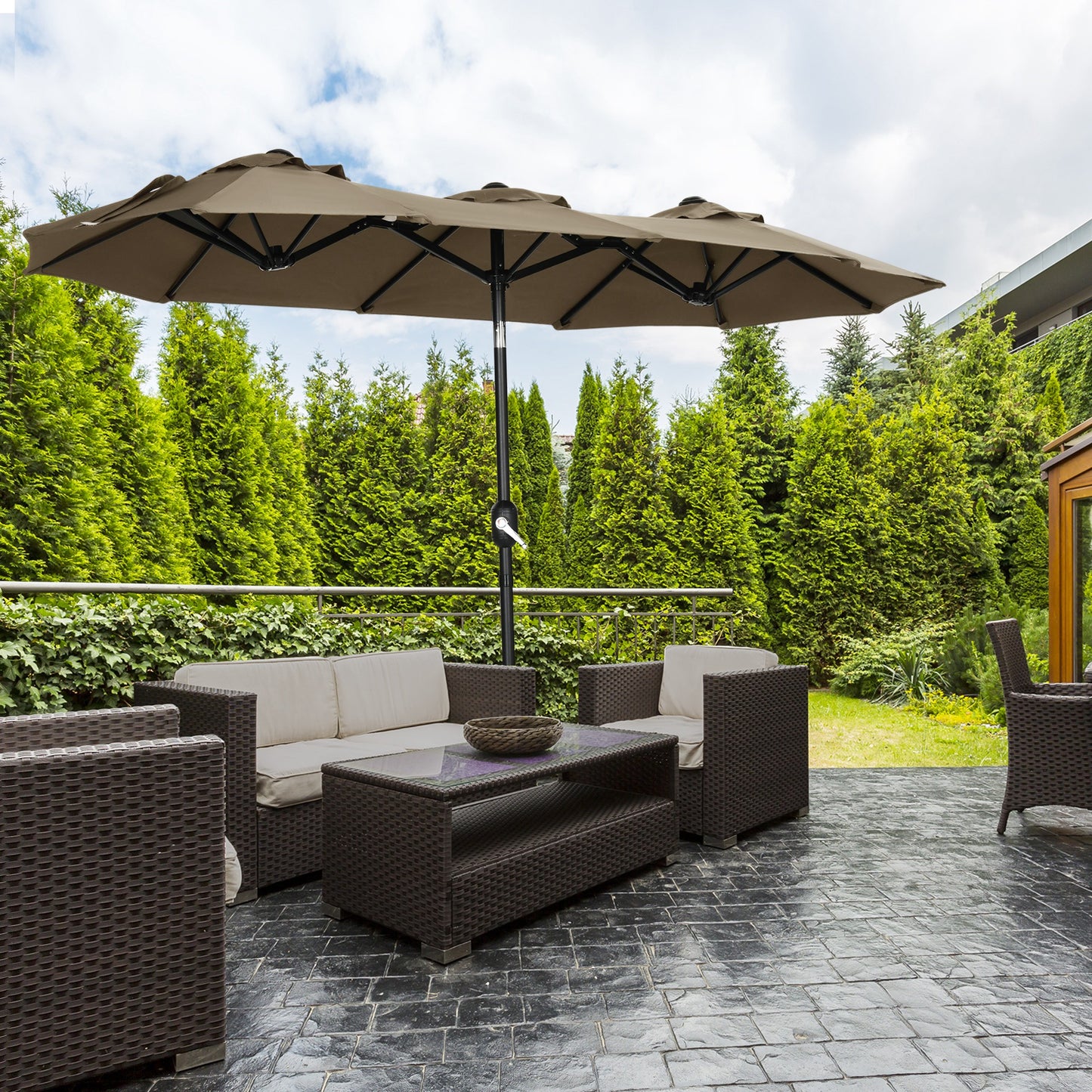 Large beige outdoor patio umbrella with brown wicker furniture set on stone patio