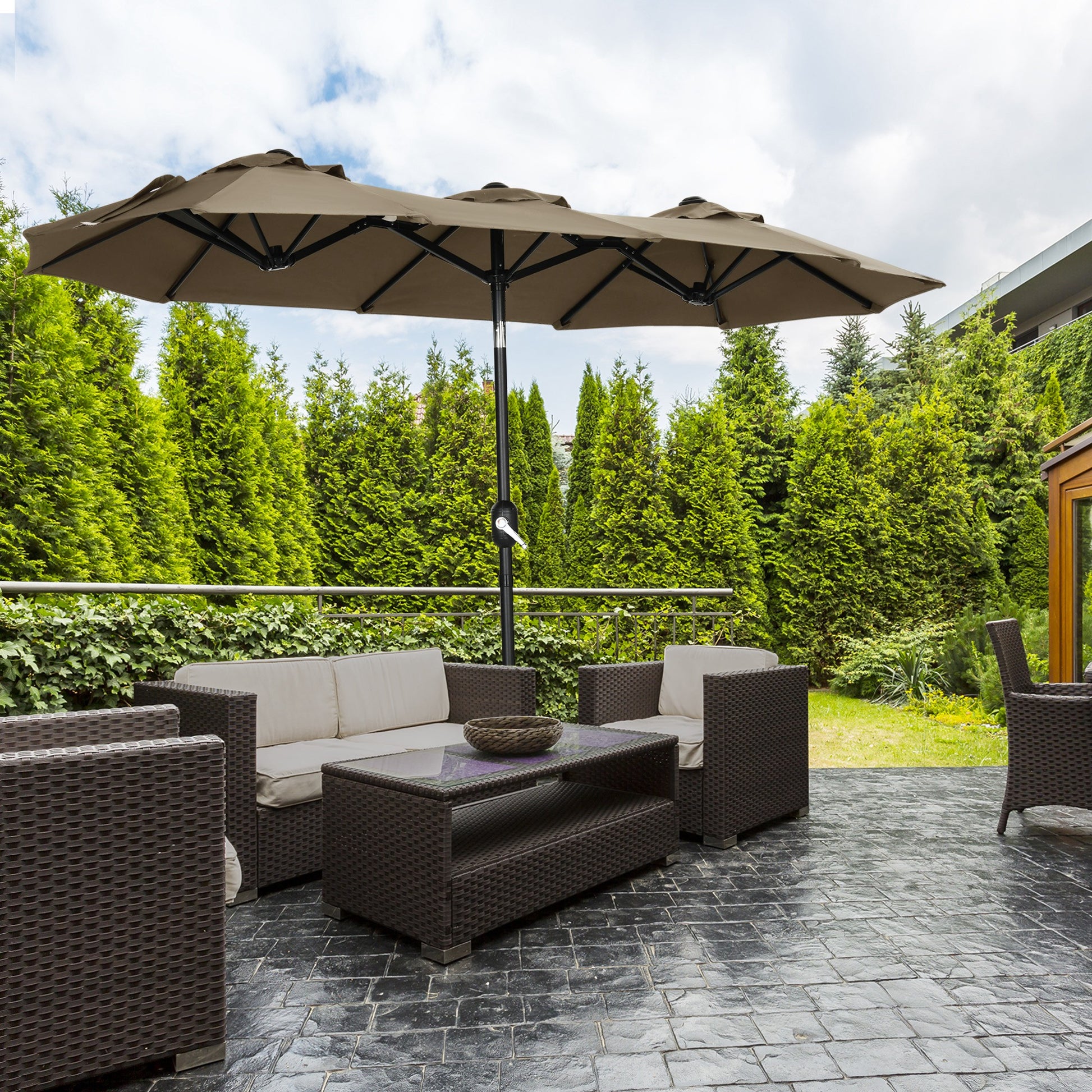 Large beige outdoor patio umbrella with brown wicker furniture set on stone patio