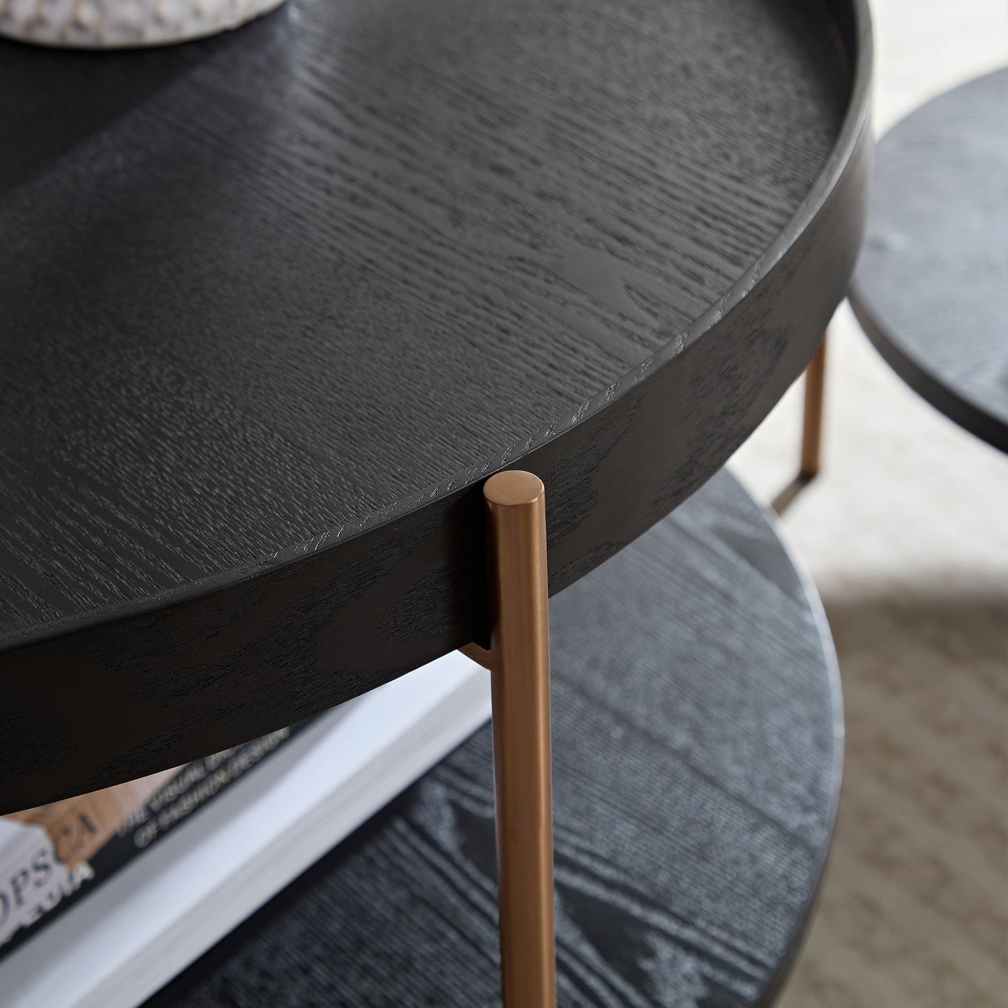 Black round nesting coffee table with textured wood grain and brass legs