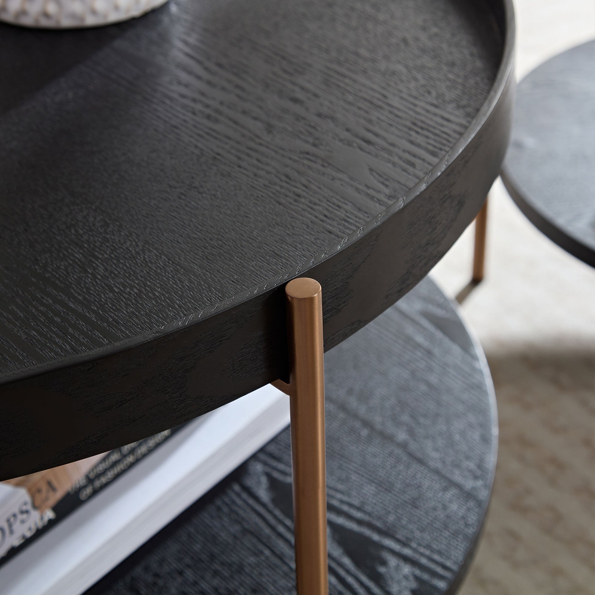 Black round nesting coffee table with textured wood grain and brass legs