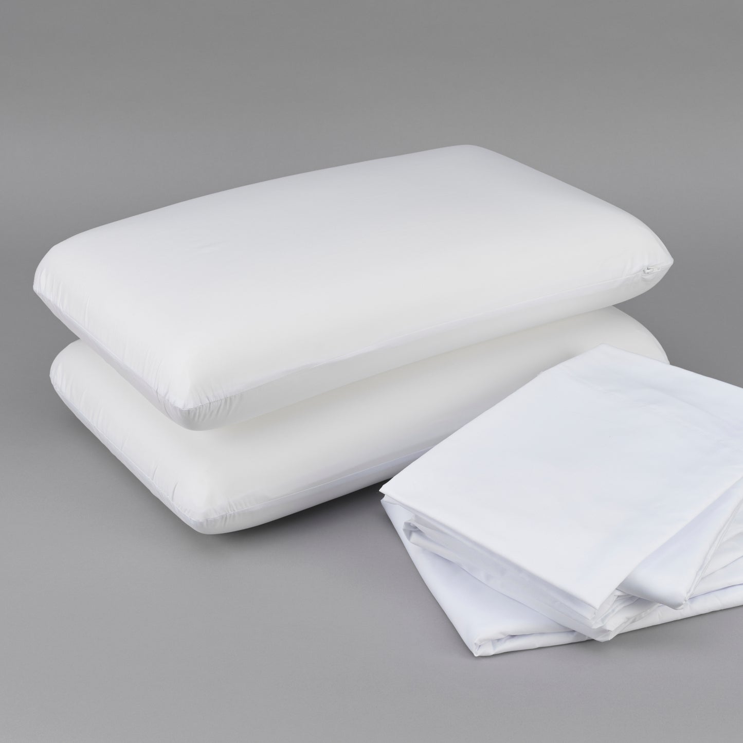 Two white down alternative pillows stacked with folded white cotton sheets on a gray background