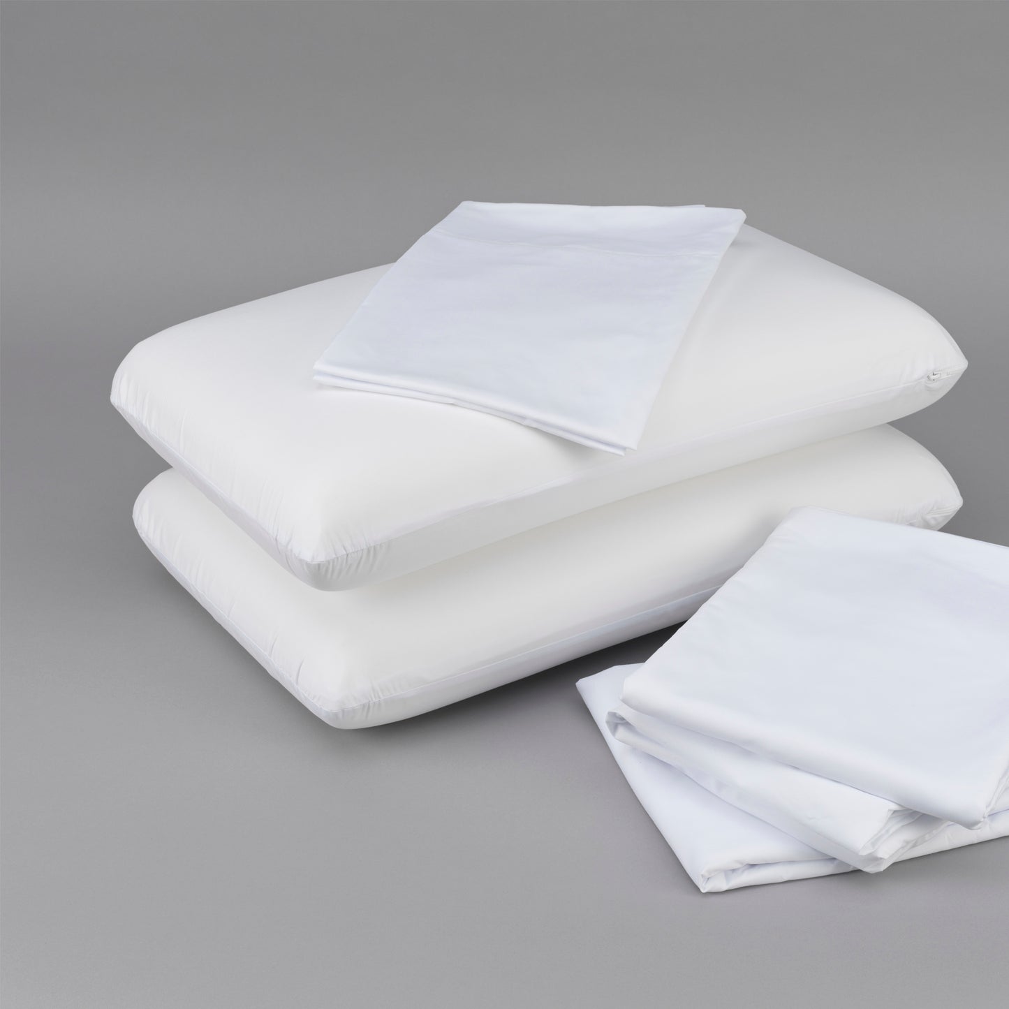 Two white cotton pillows with folded white cotton pillowcases on a gray background