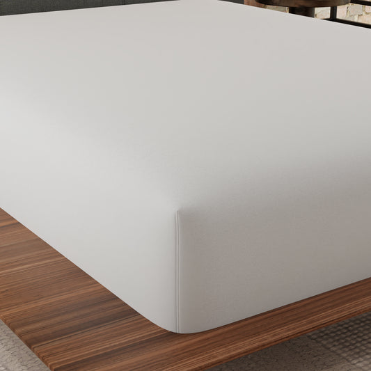 Closeup of a white fitted sheet with a textured surface draped over a mattress