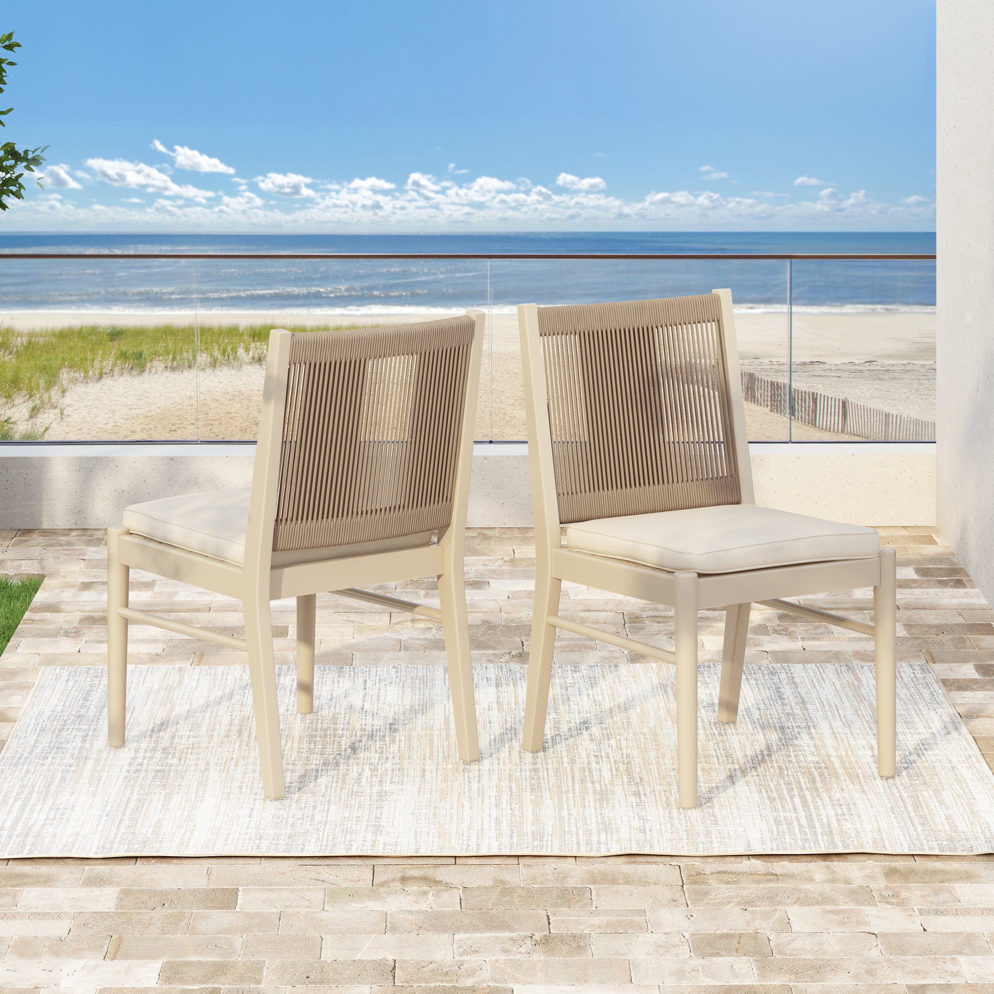 Two beige outdoor dining chairs with rope backs and cream cushions on a patio overlooking the ocean