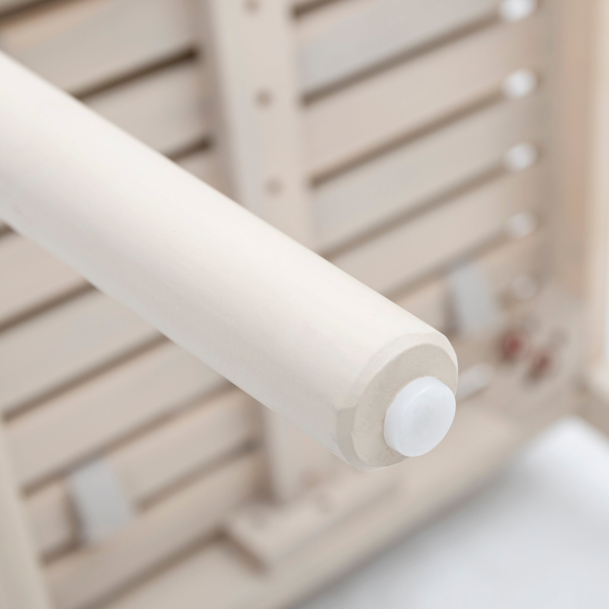 Closeup of a white wooden dowel rod with a protective cap part of a slatted shelf