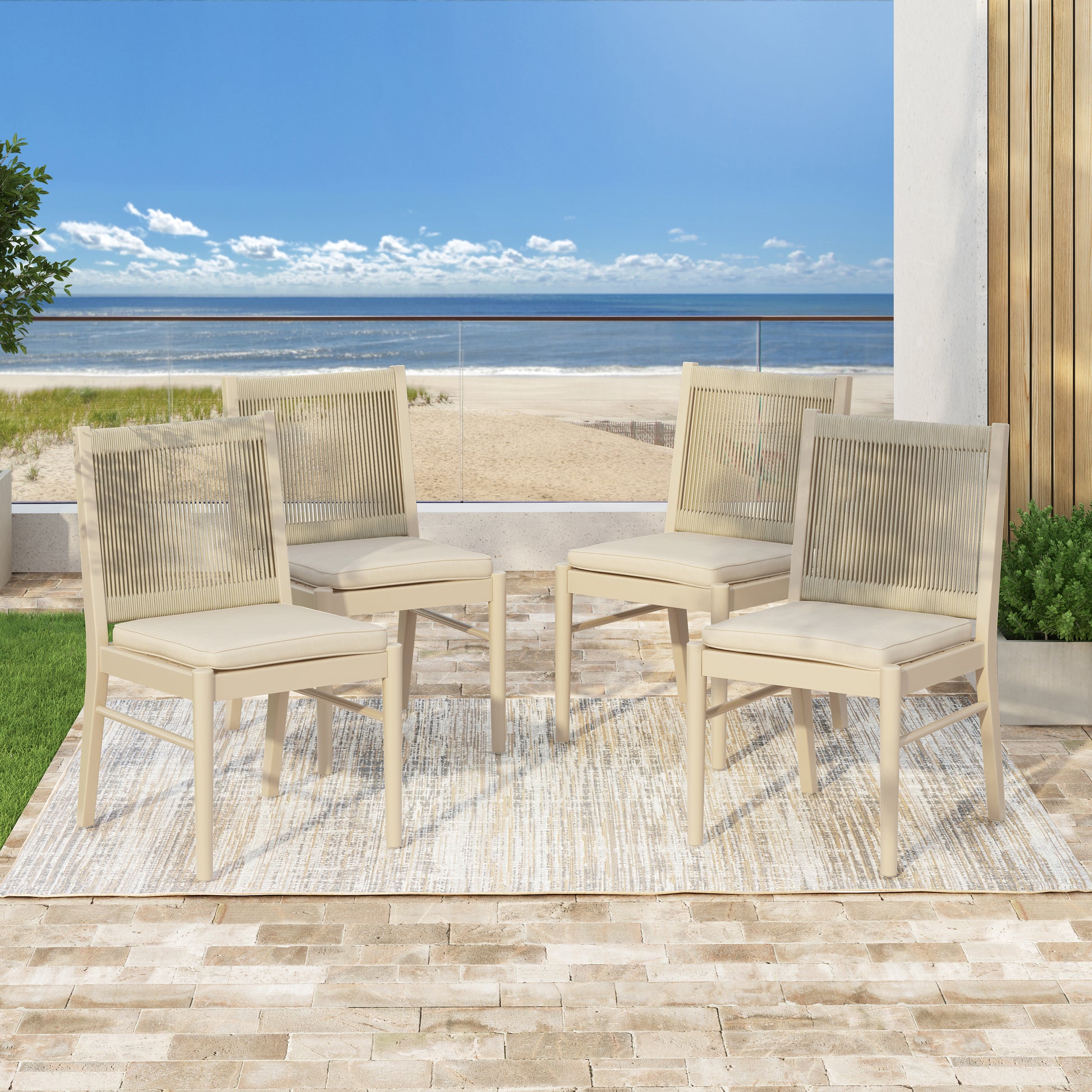 Four beige woven back dining chairs with beige cushions on a patio rug with ocean view
