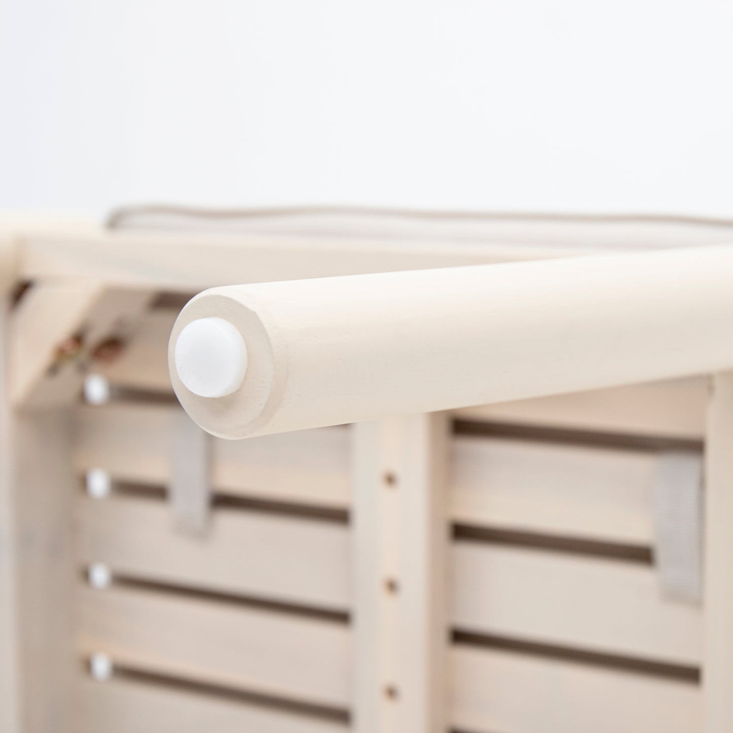 Closeup of a light wood bed frame rail with a white protective cap