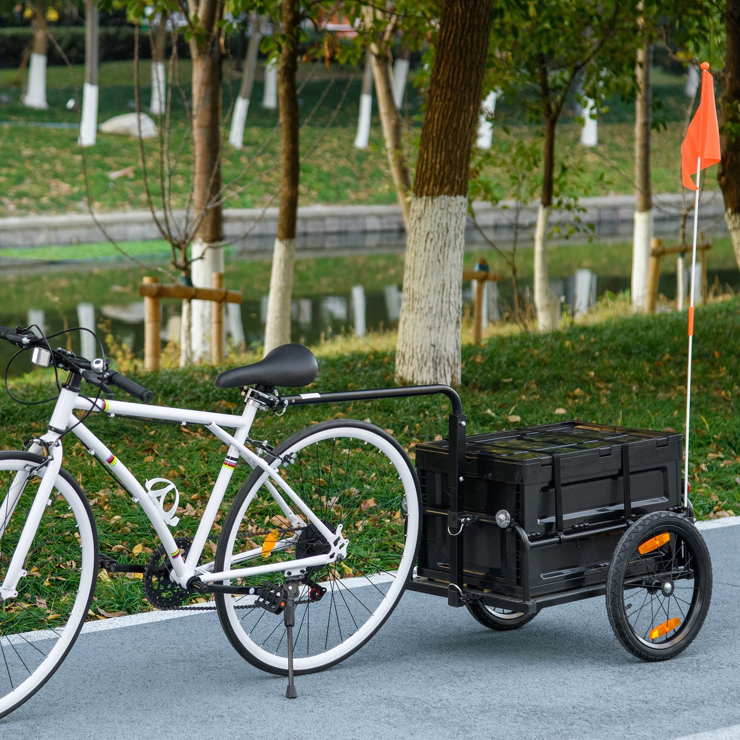 White bicycle with black cargo trailer featuring a large black storage box and an orange safety flag