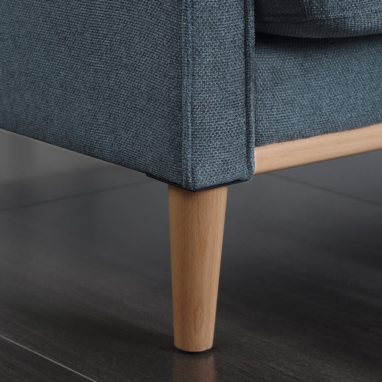 Closeup of a dark teal fabric sofa arm with a tapered wooden leg