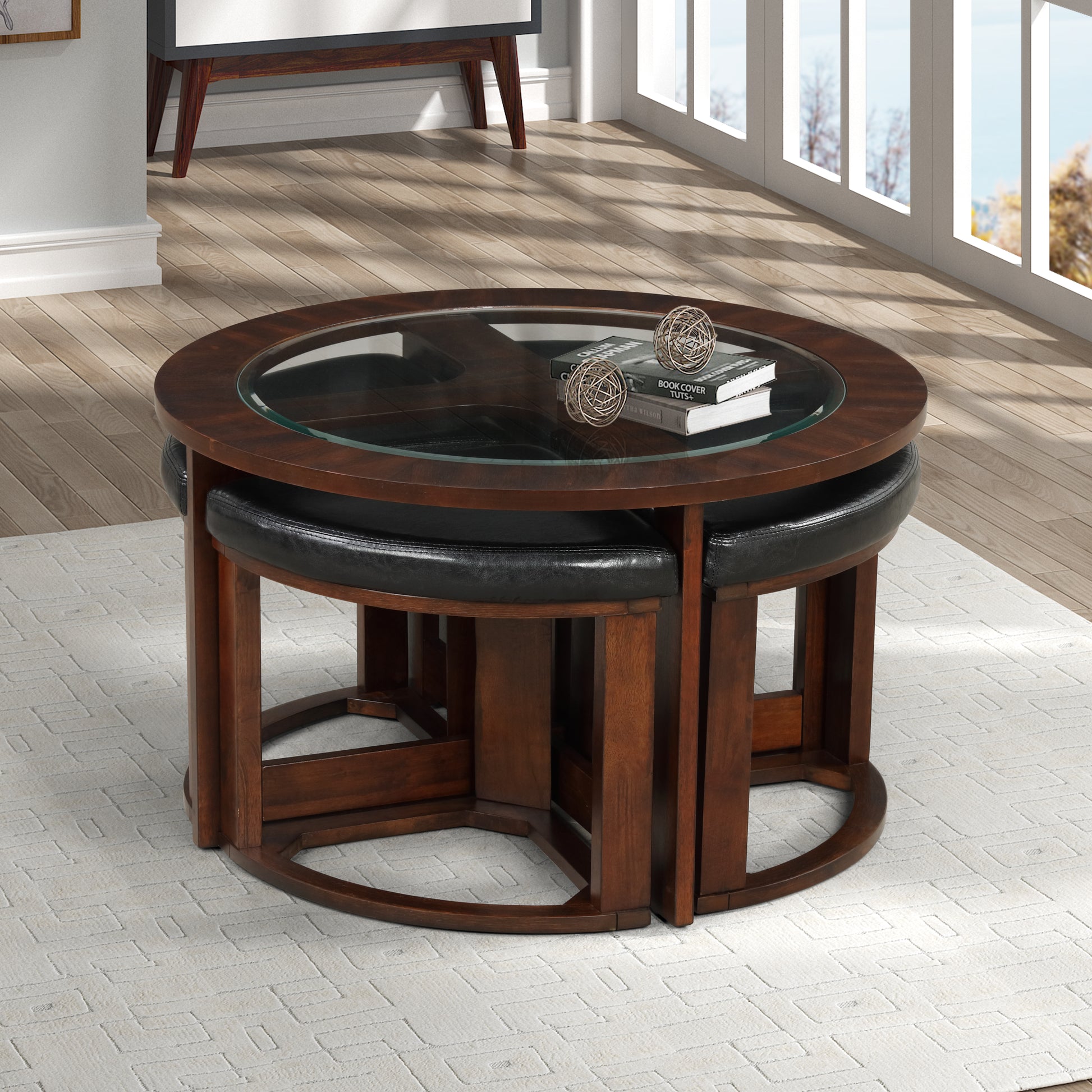 Round wooden coffee table with glass top and four black leather ottomans nested underneath