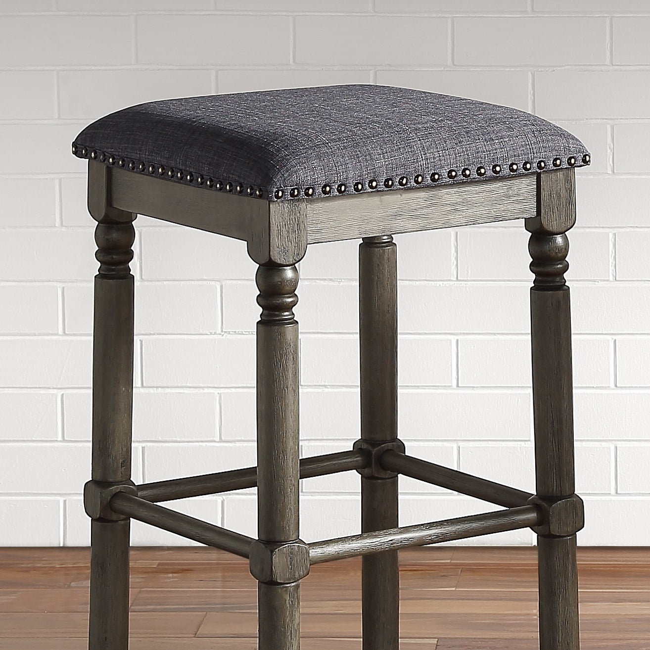 Upholstered grey bar stool with decorative nailhead trim and turned wooden legs