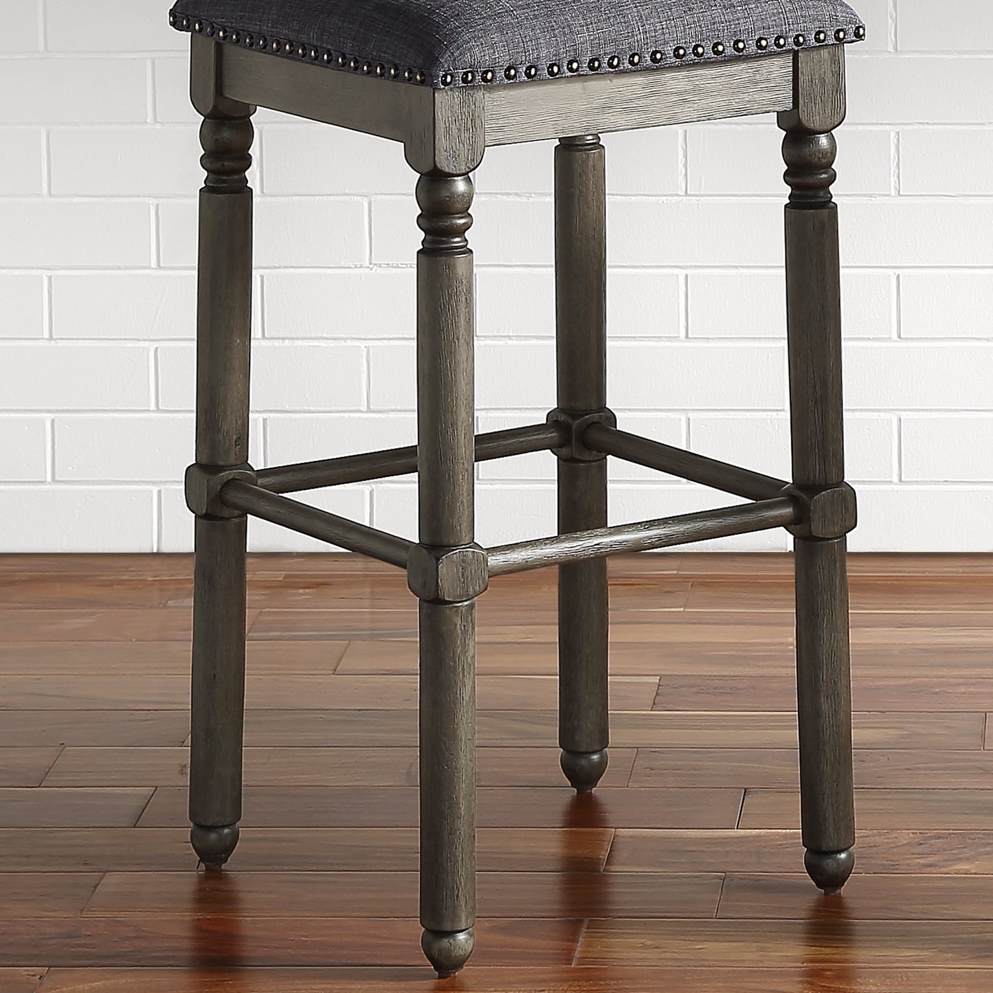 Dark gray upholstered bar stool with nailhead trim and turned wooden legs on a wooden floor