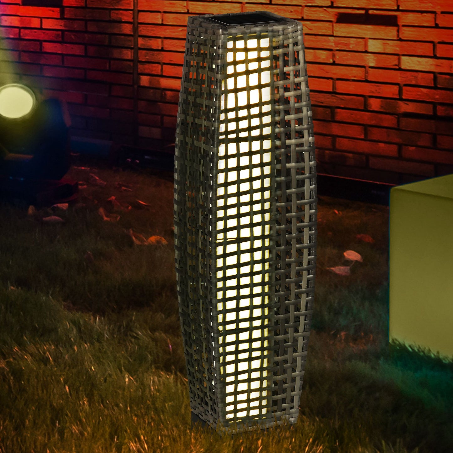 Tall grey wicker outdoor lantern with internal light source set on grass at night