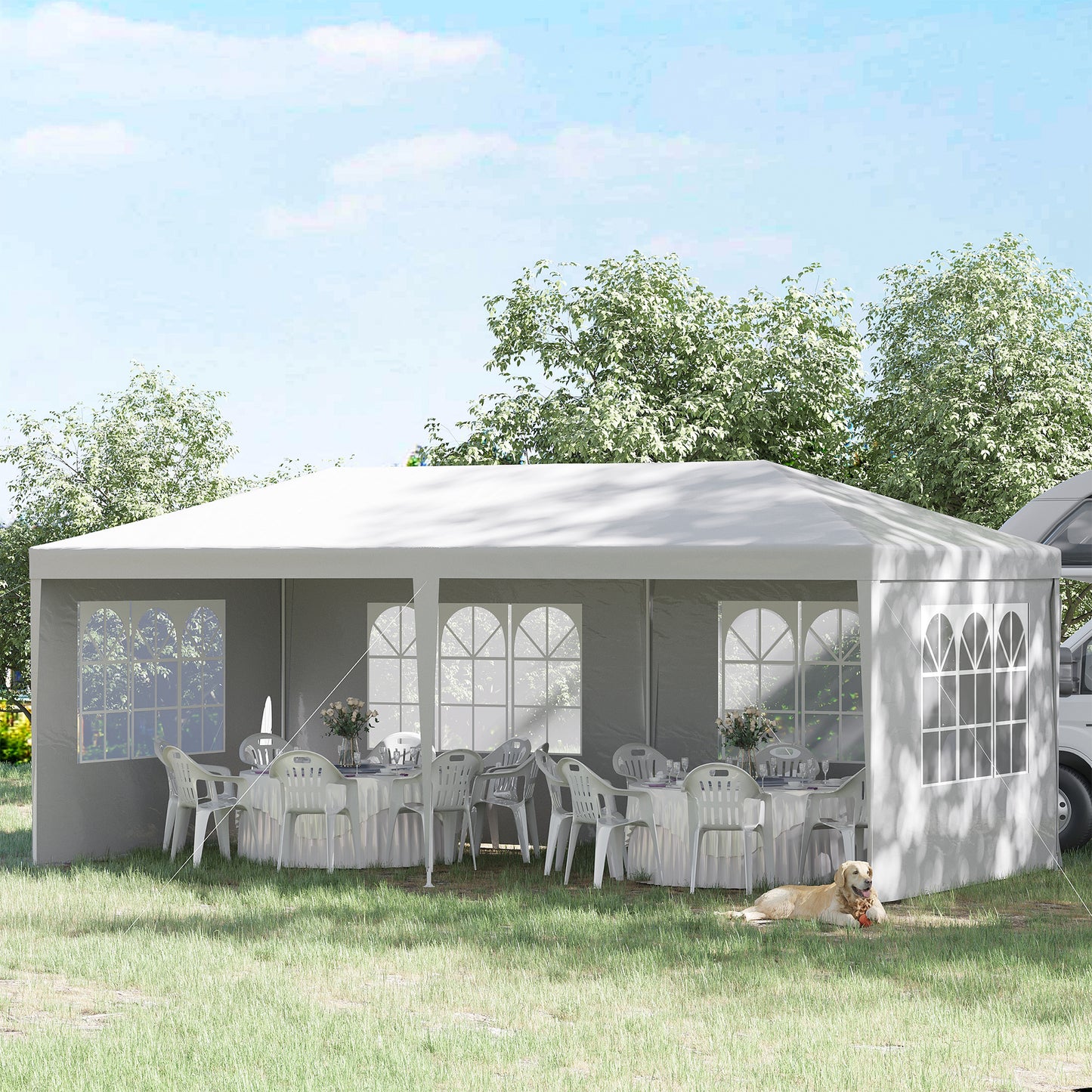 Large white party tent set up on grass with tables chairs and a dog