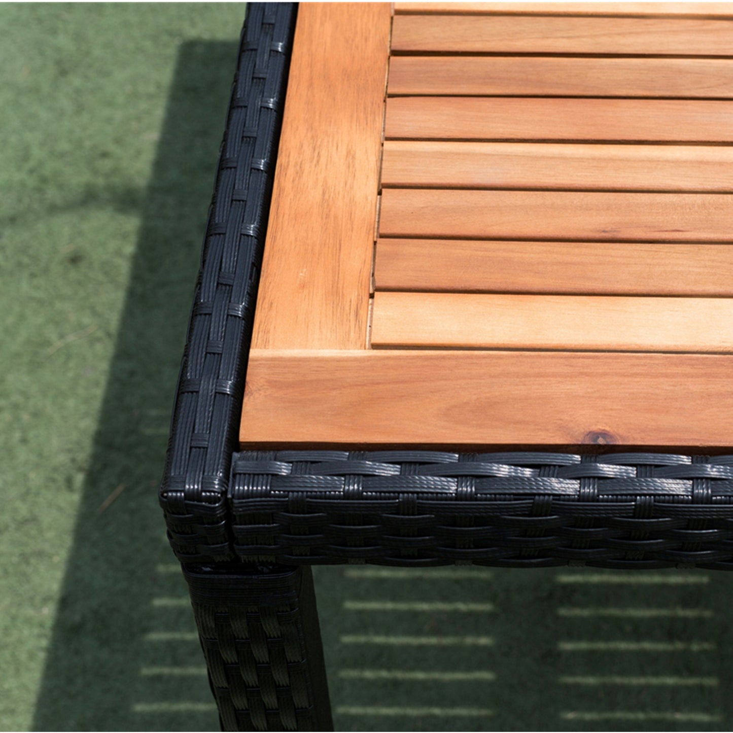 Closeup of a patio table corner natural wood slats atop woven black wicker frame