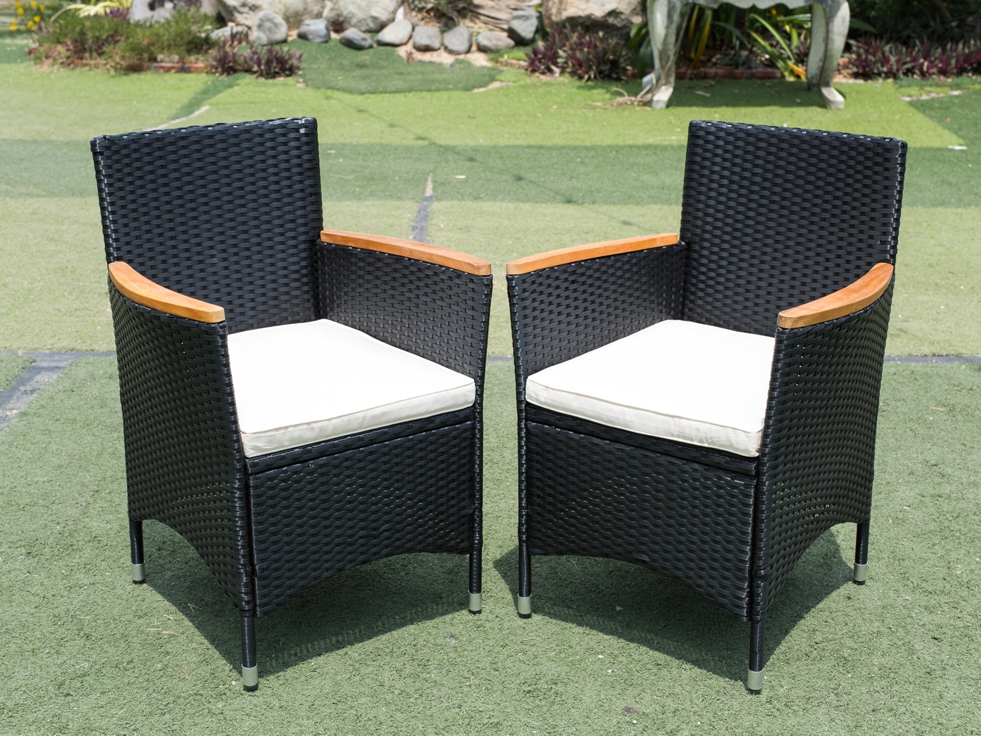 Two black wicker patio chairs with light beige cushions and wood armrests
