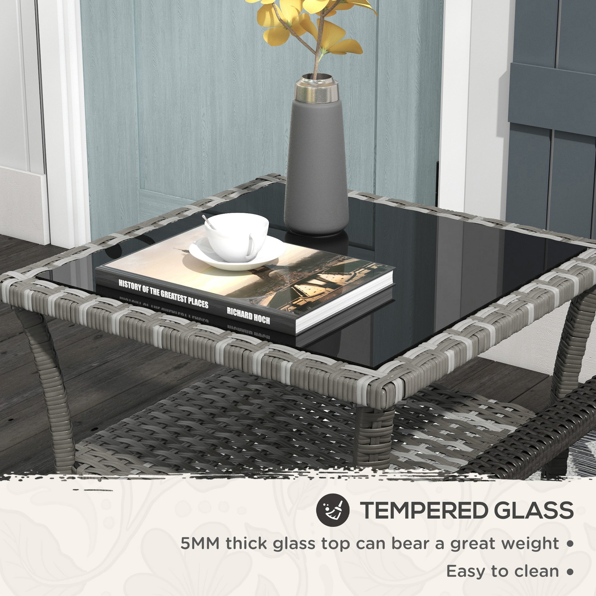 Gray rattan side table with tempered glass top holding books and cup