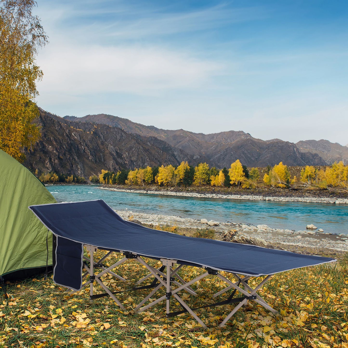 Navy blue foldable camping cot set up by a river with mountains in the background