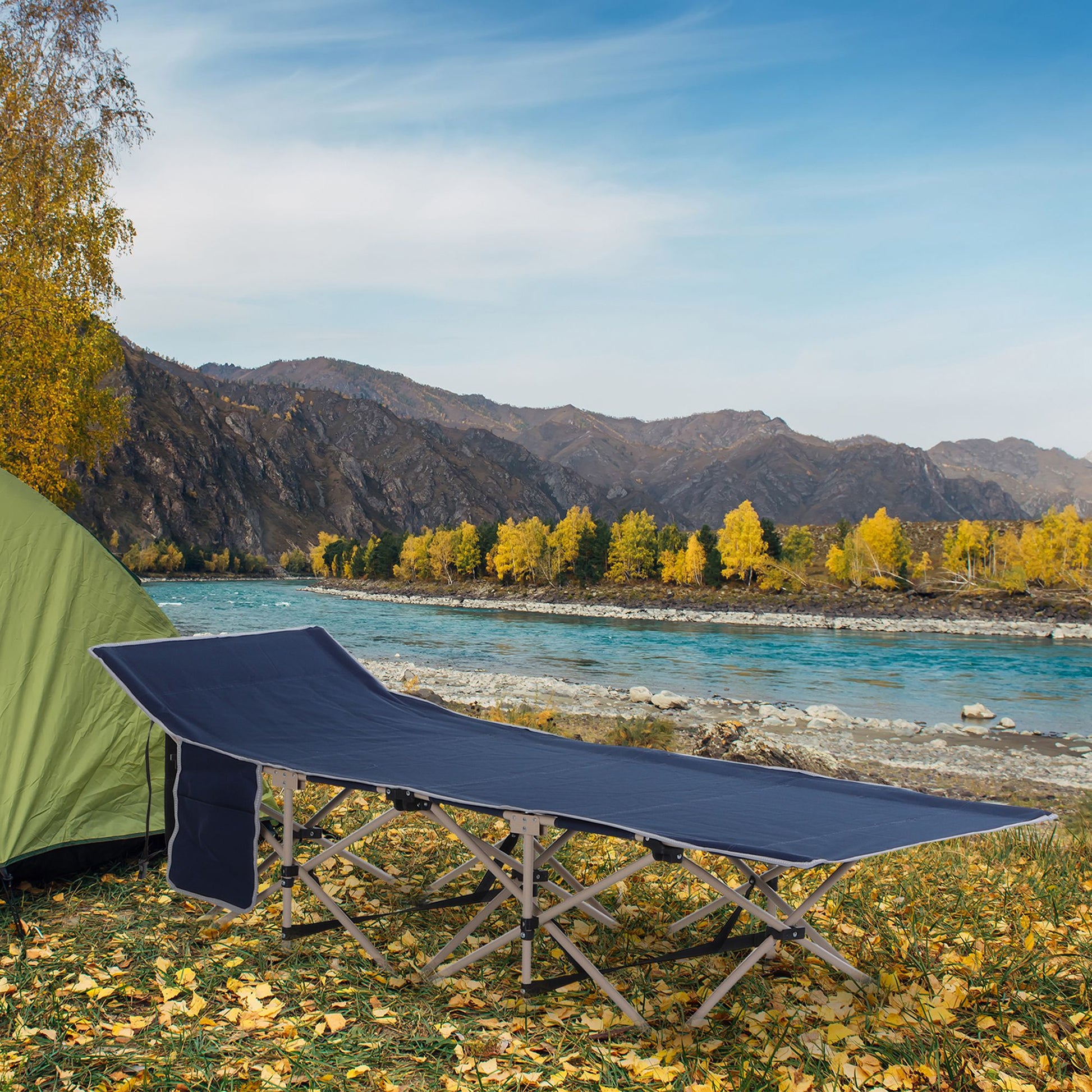 Navy blue foldable camping cot set up by a river with mountains in the background