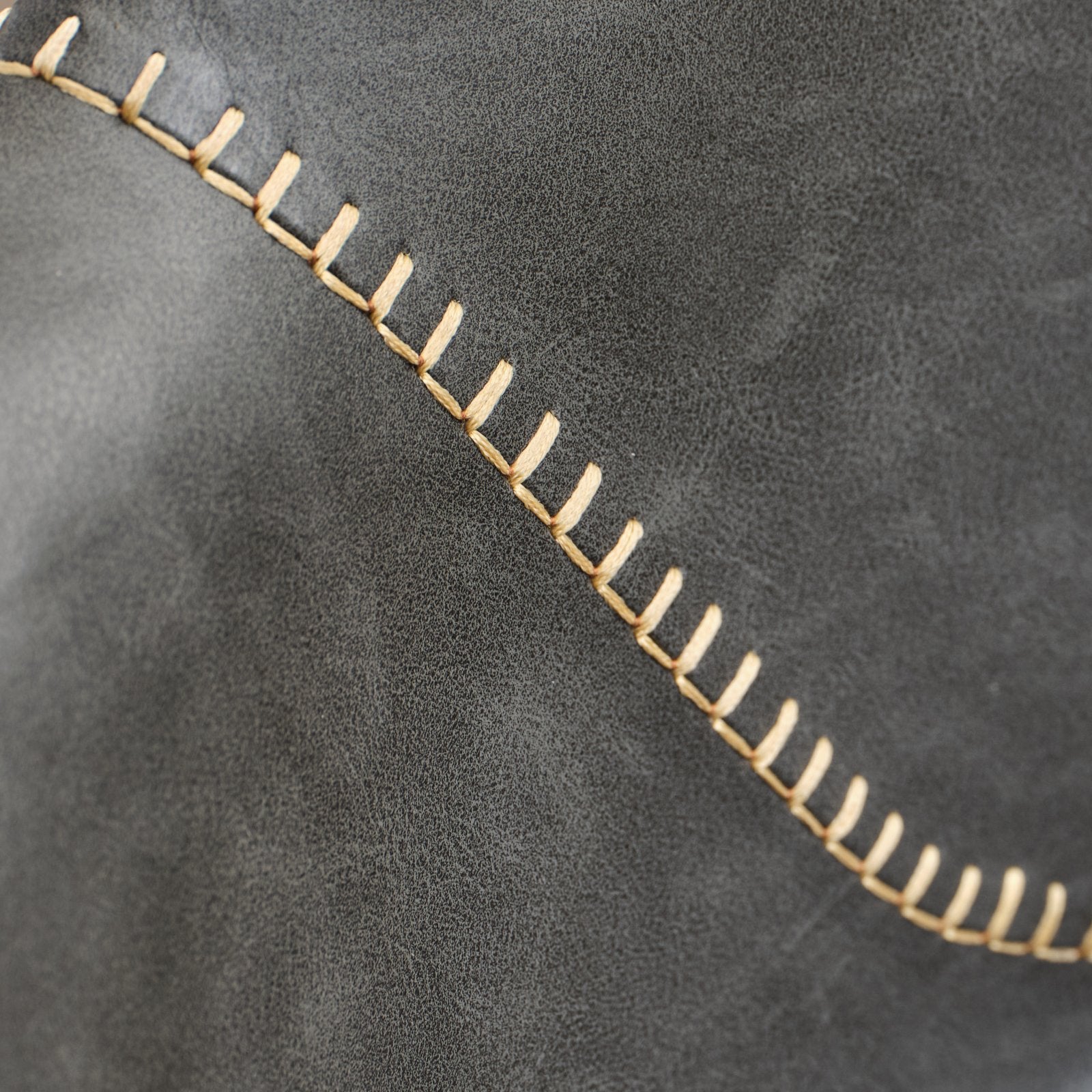 Closeup of dark grey faux leather with contrasting beige stitching along a diagonal seam