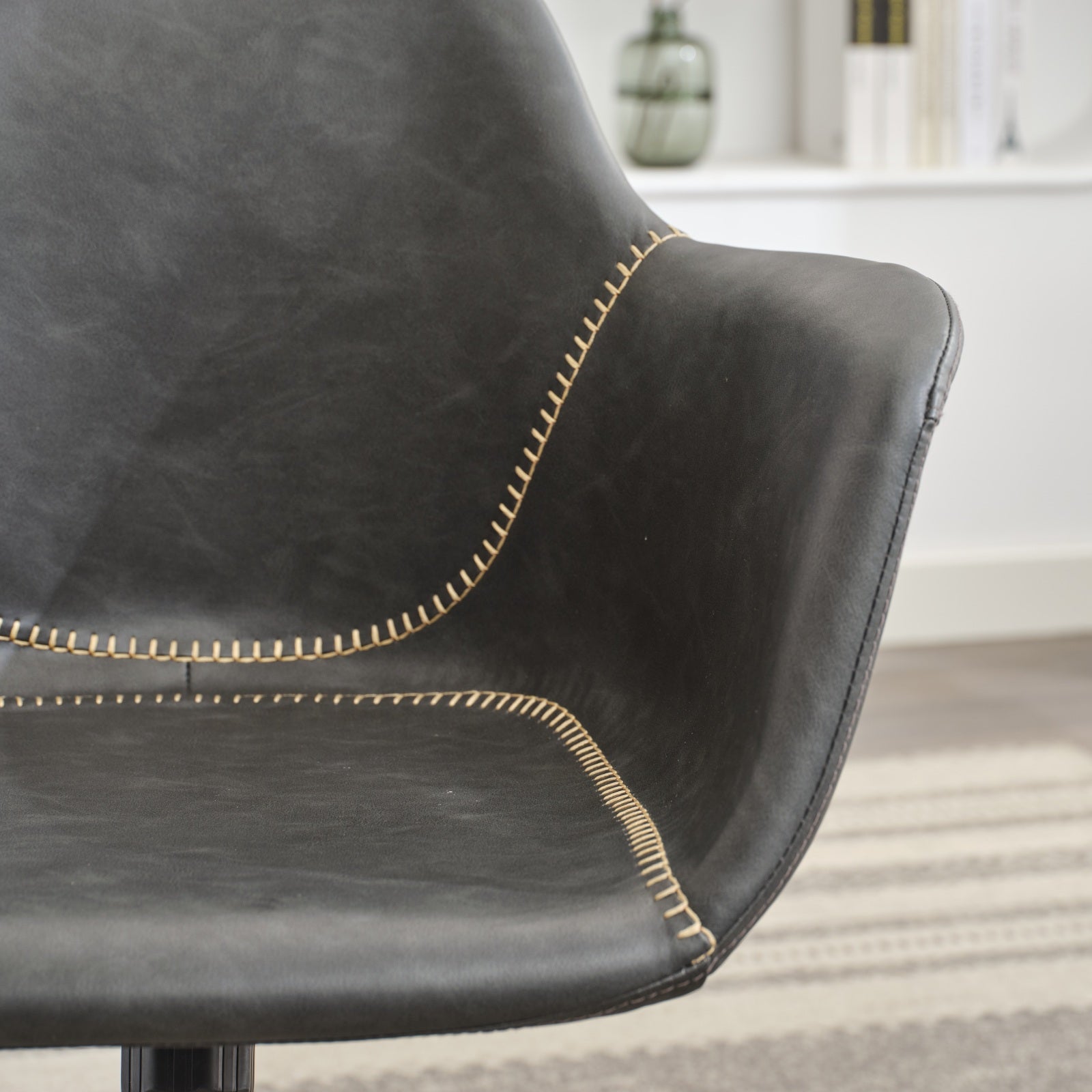 Closeup of a dark grey faux leather chair with contrasting tan stitching offering a modern accent