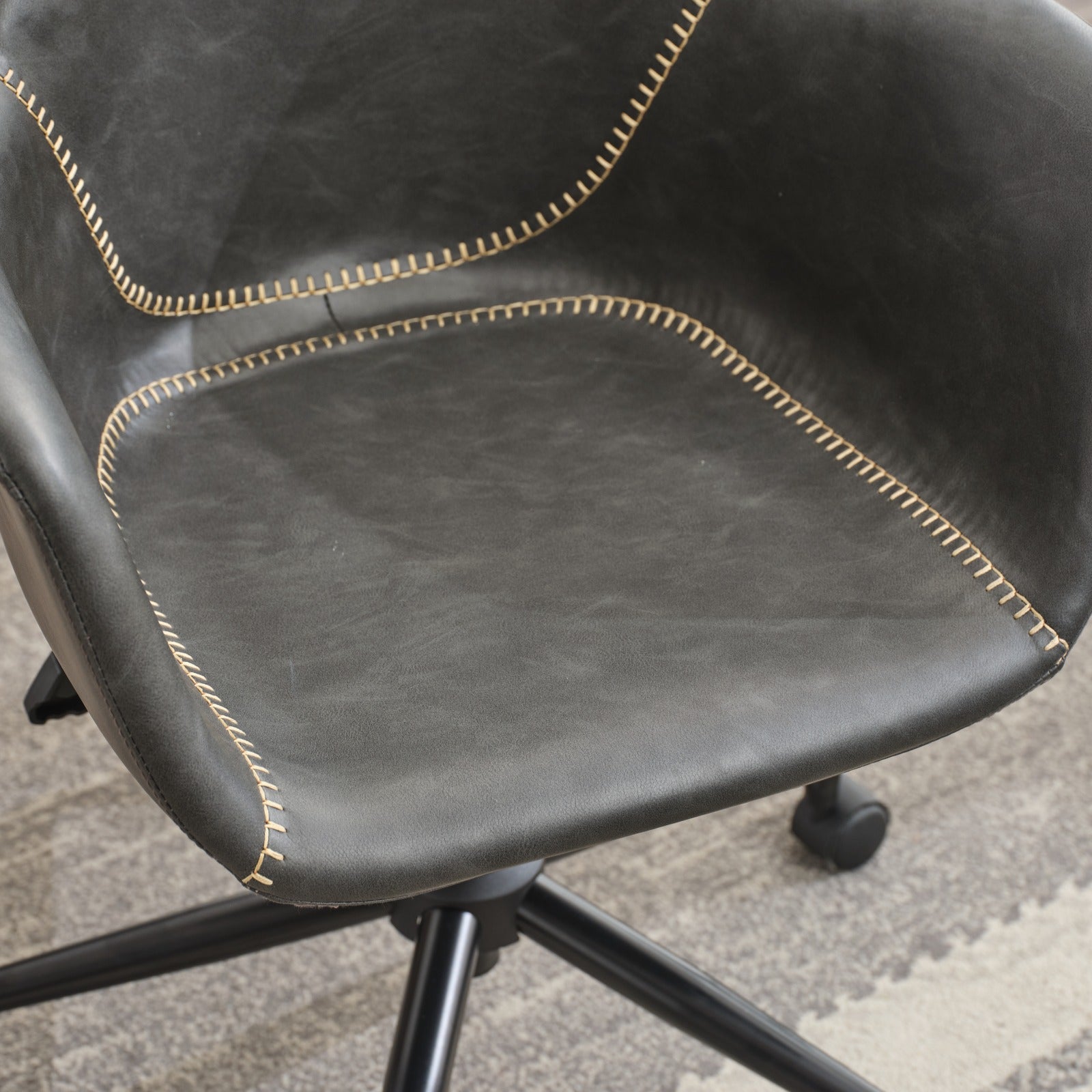 Closeup of a dark gray upholstered office chair with contrasting stitching and a wheeled base