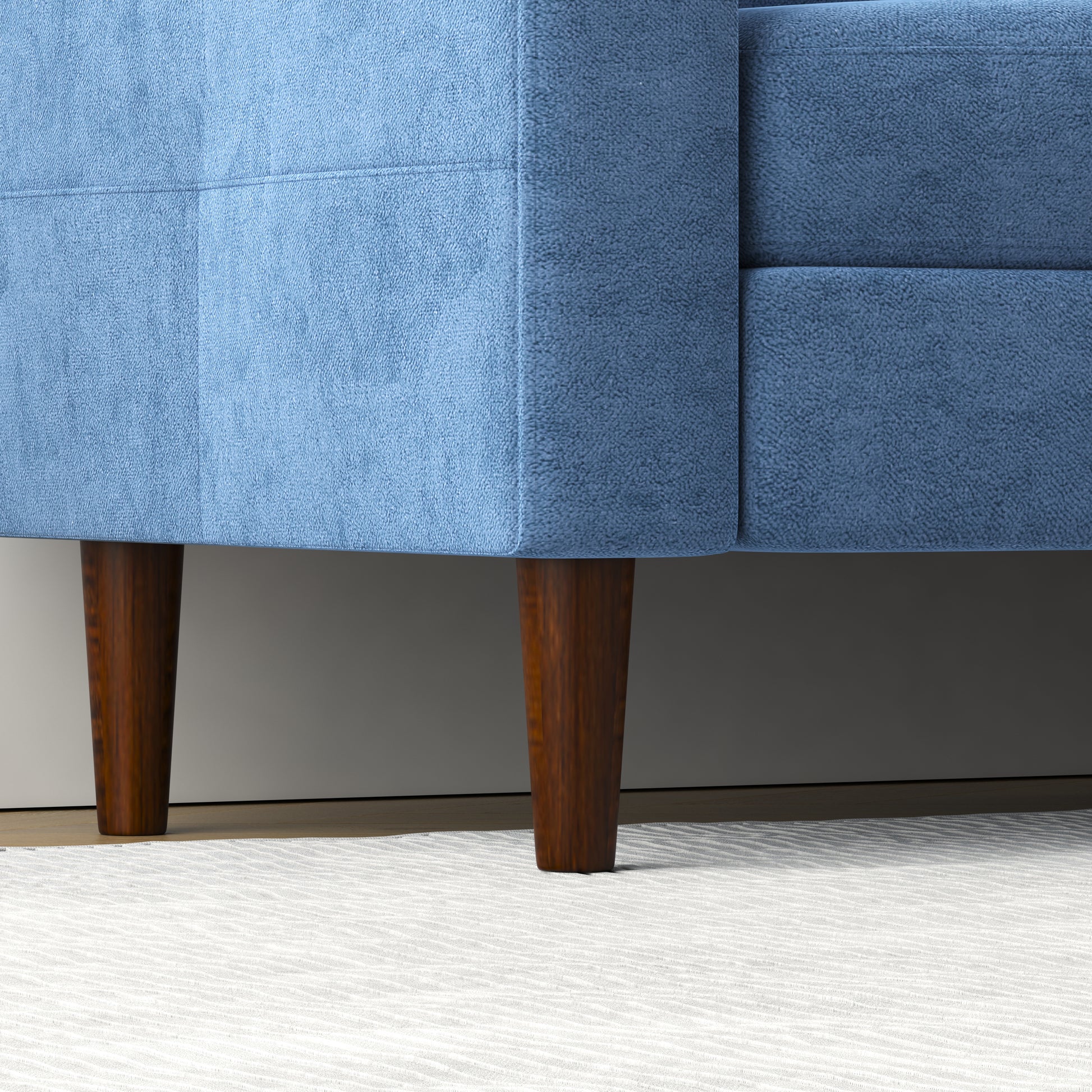 Closeup of a blue fabric sofa with angled wooden legs on a textured rug