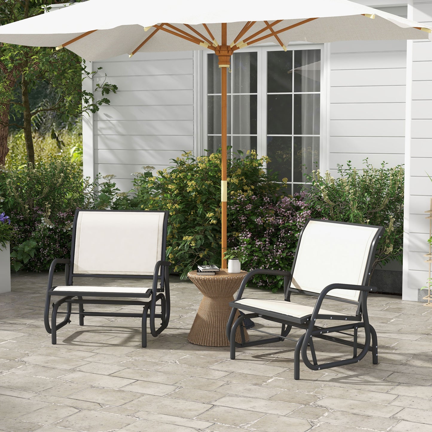Two charcoal metal outdoor gliders with cream cushions near wicker side table