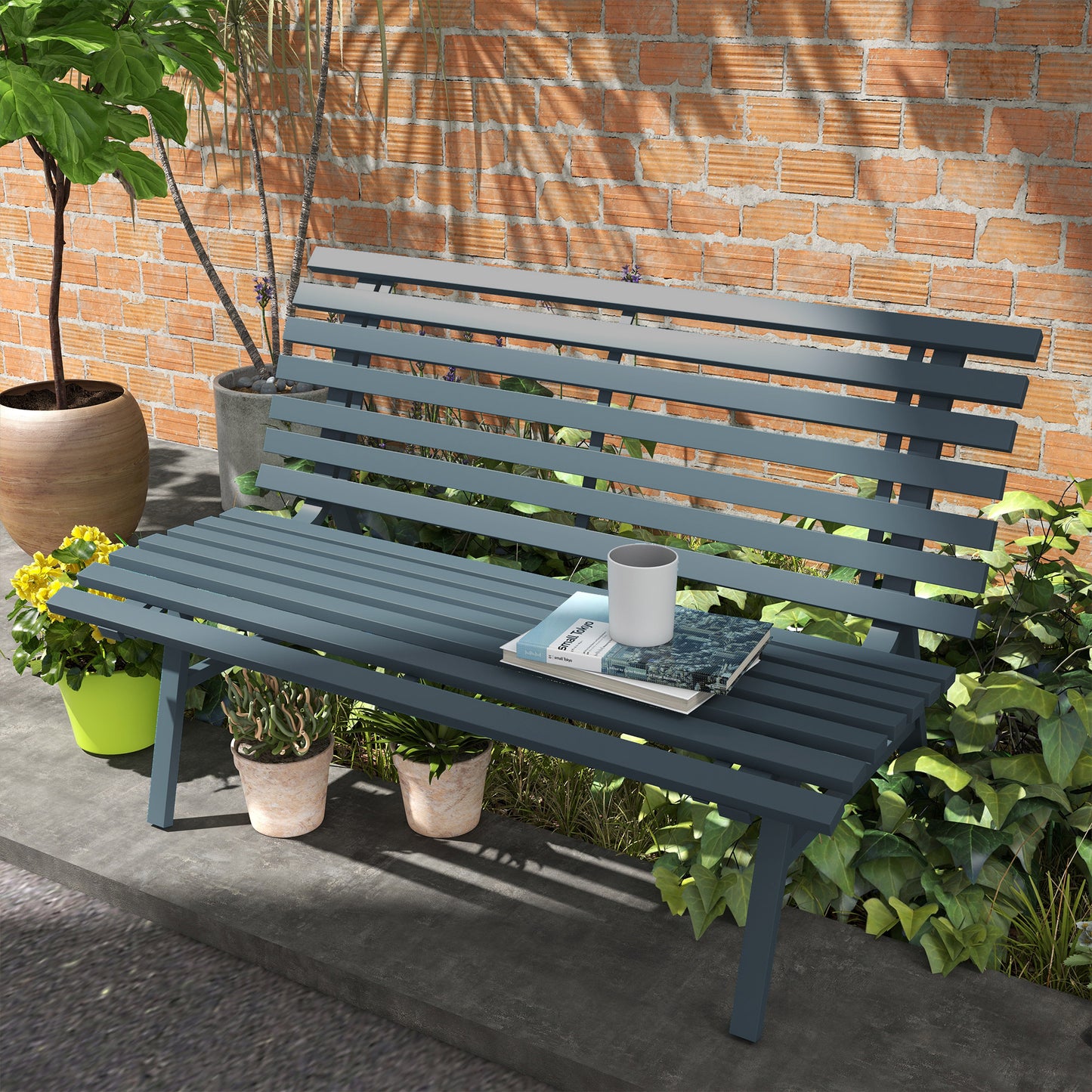 Dark gray metal slatted park bench with a white mug and books on the seat set against a brick wall