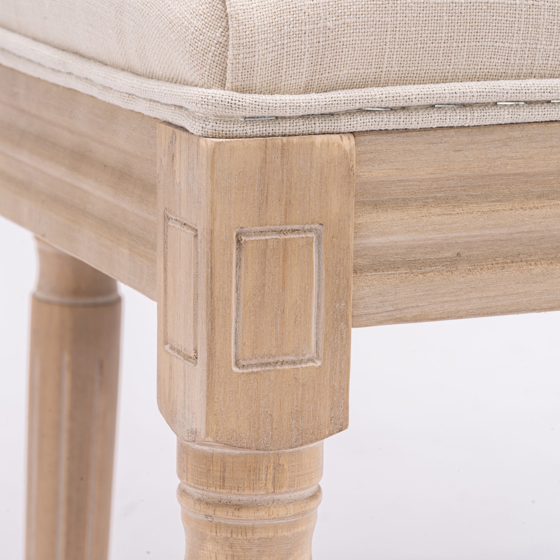 Closeup of a beige upholstered bench seat with a distressed wood frame and carved detailing