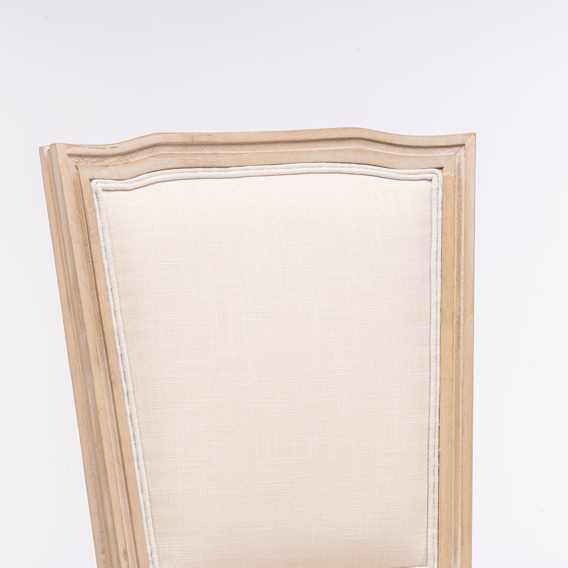 Closeup of a beige upholstered chair back with a distressed light wood frame