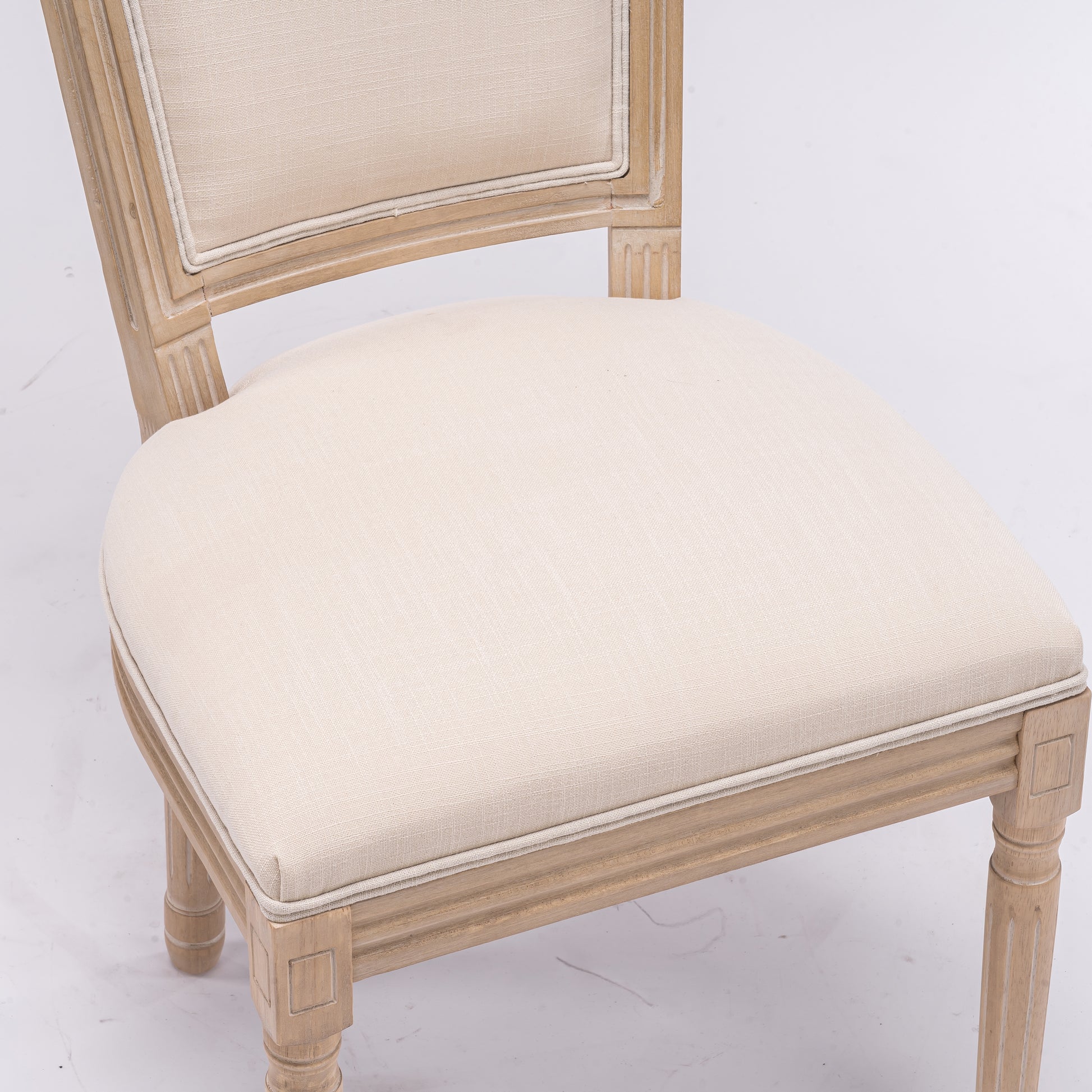 Light beige linen upholstered dining chair with distressed wood frame and carved details