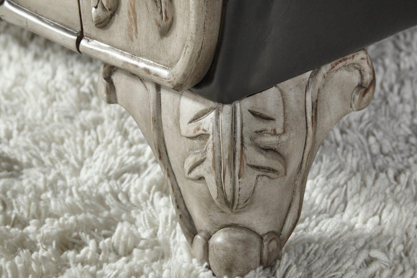 Ornate carved wood furniture leg with distressed ivory finish on plush white rug