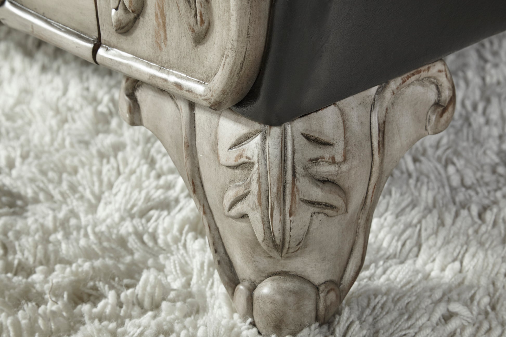 Ornate carved wood furniture leg with distressed ivory finish on plush white rug