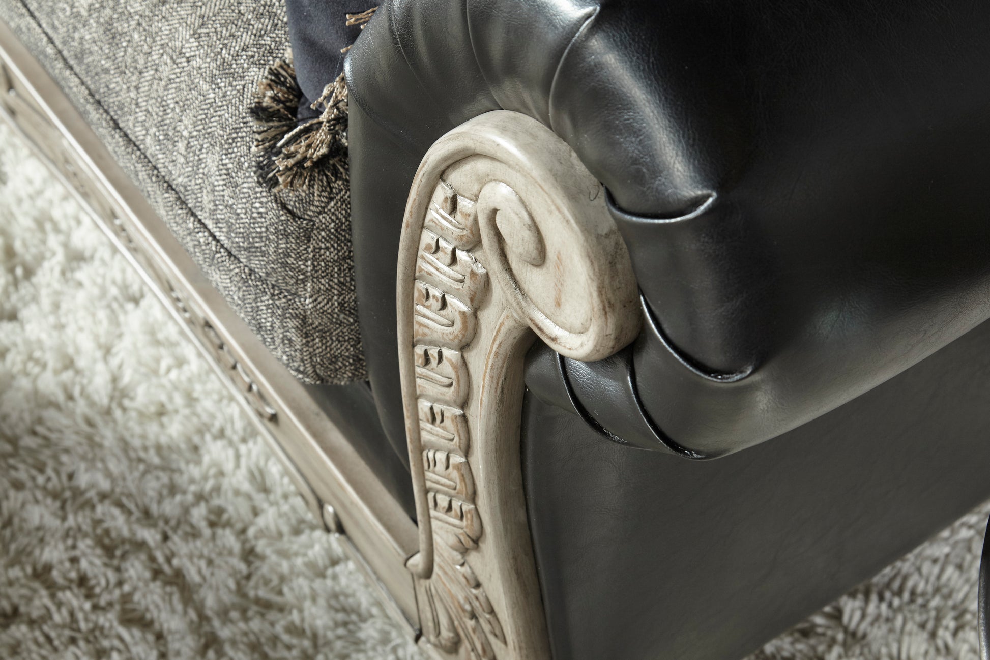 Black leather sofa arm with carved wood trim and textured throw pillow