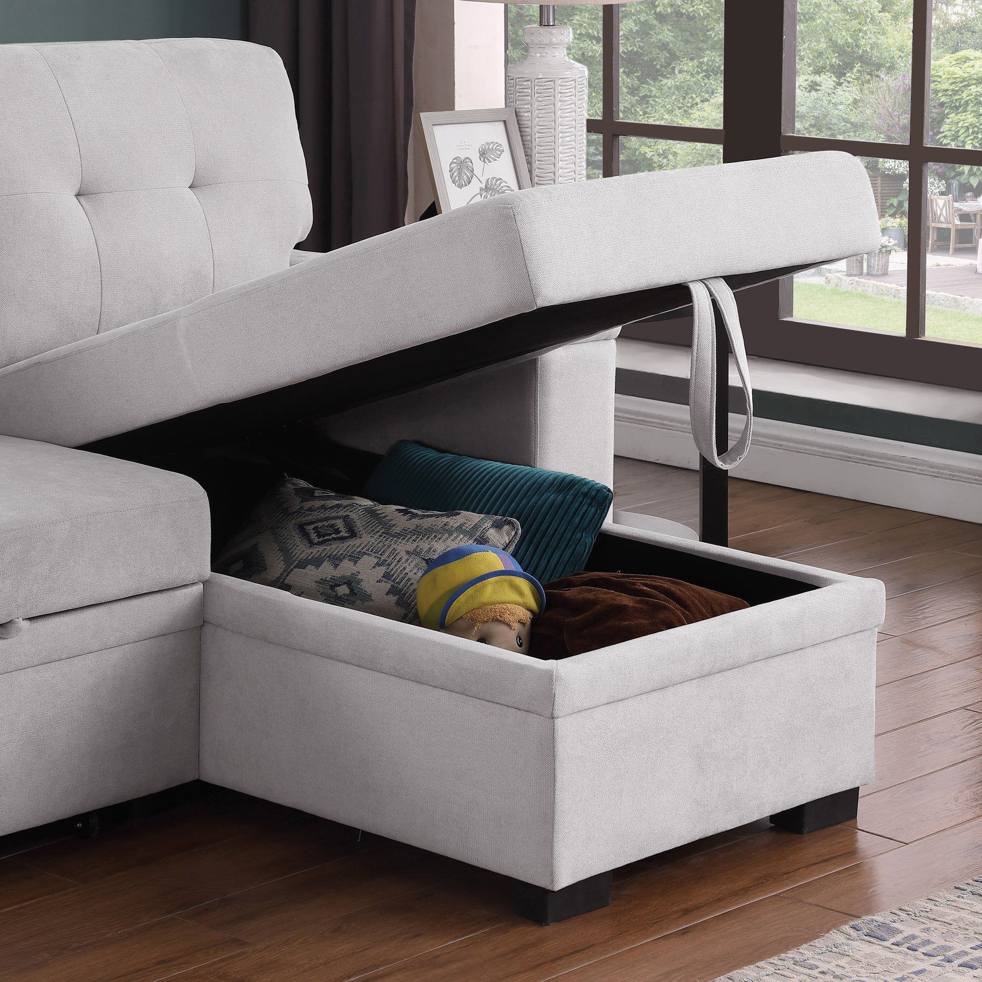 Light gray sectional sofa with open storage revealing pillows and a doll