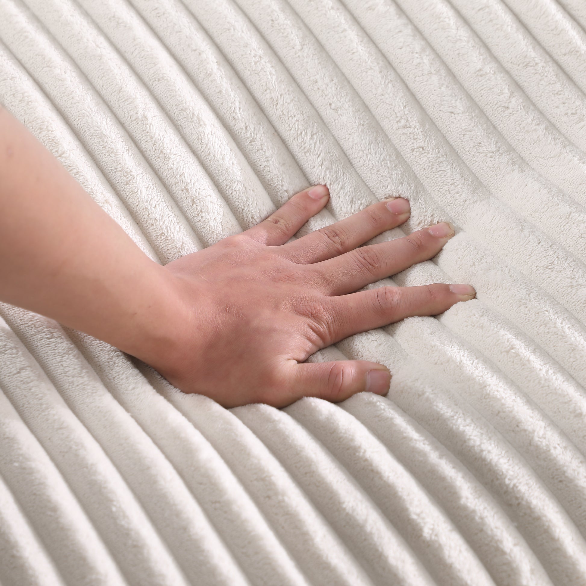 Closeup of hand pressing into plush creamcolored corduroy fabric for comfort and texture