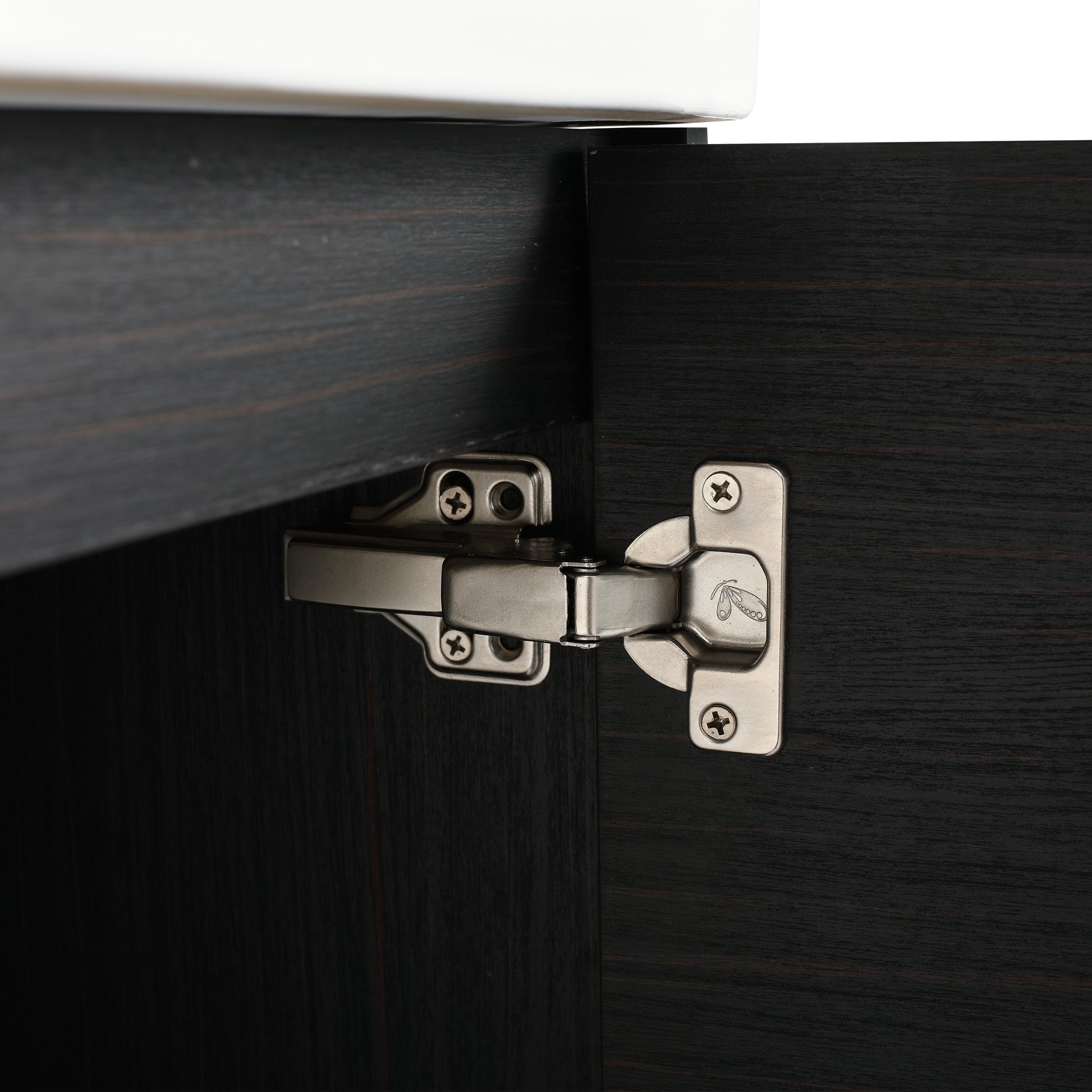 Closeup of a brushed nickel cabinet hinge attached to dark wood grain cabinetry