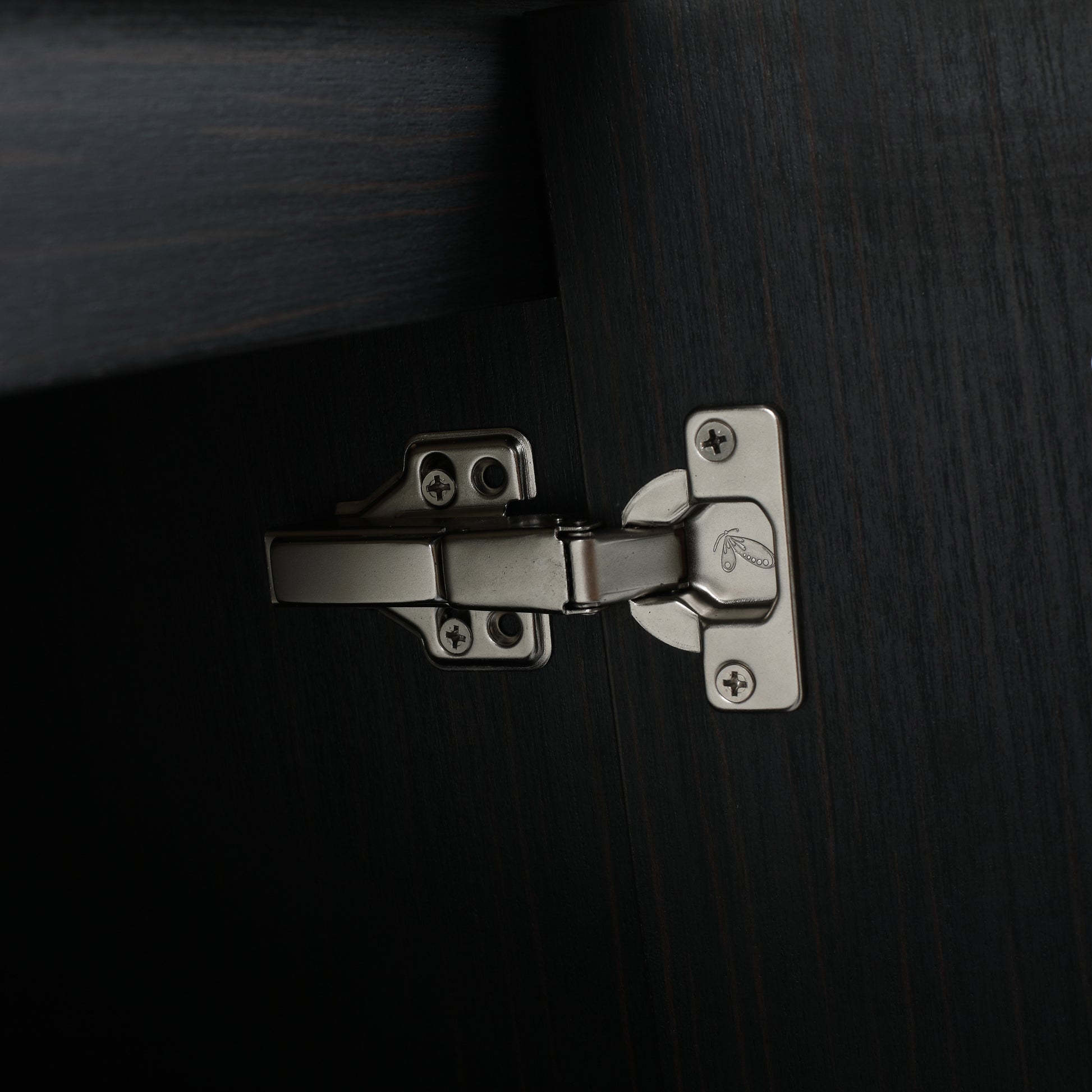 Closeup of a brushed nickel cabinet hinge attached to dark wood for furniture assembly