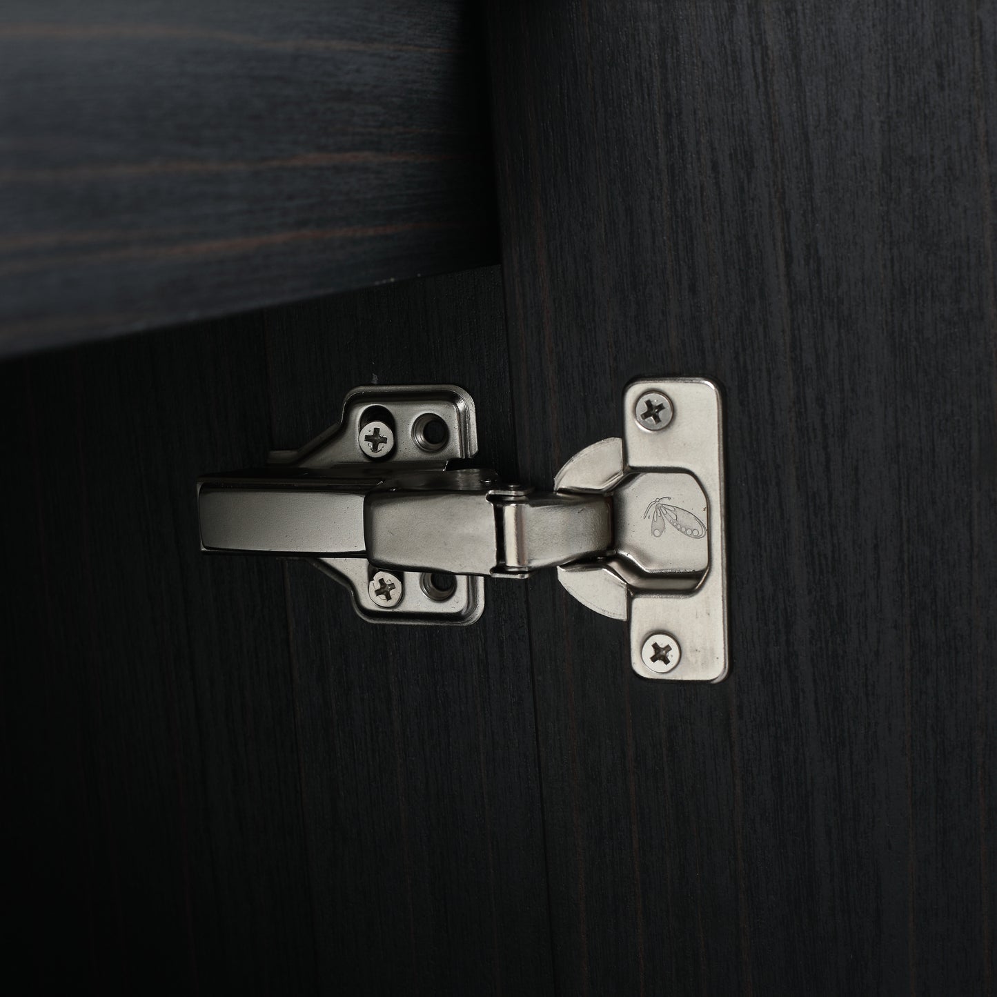 Closeup of a silver concealed cabinet hinge with screws on dark wood grain