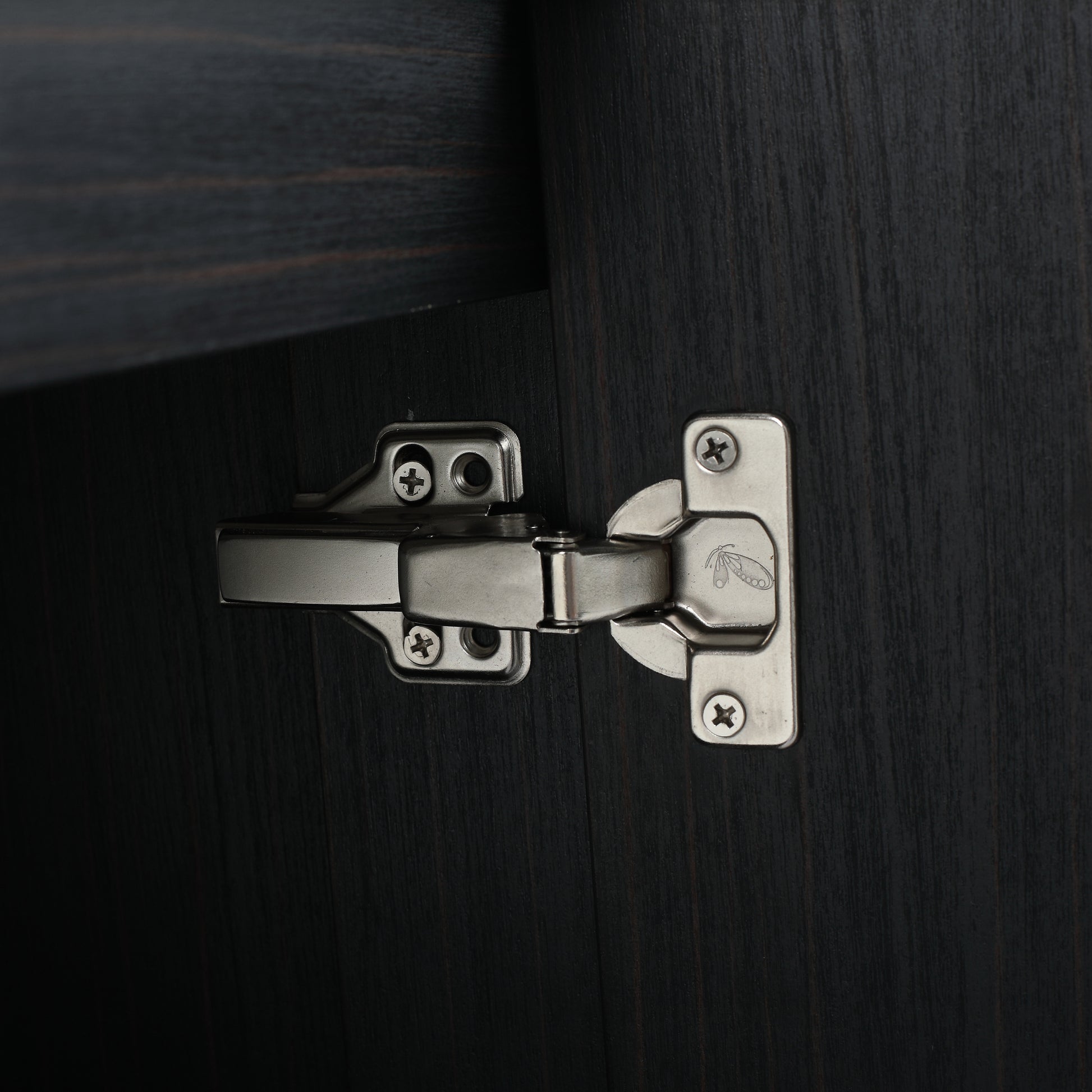 Closeup of a silver concealed cabinet hinge with screws on dark wood grain