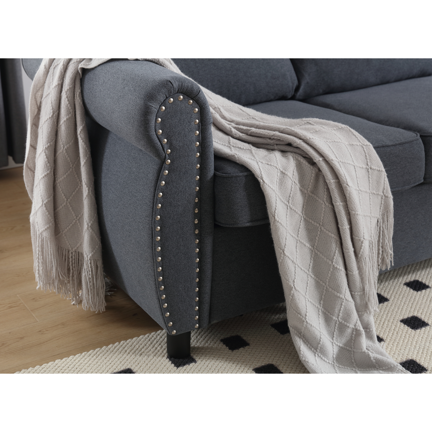 Dark grey upholstered sofa with silver nailhead trim and a cream knit throw blanket