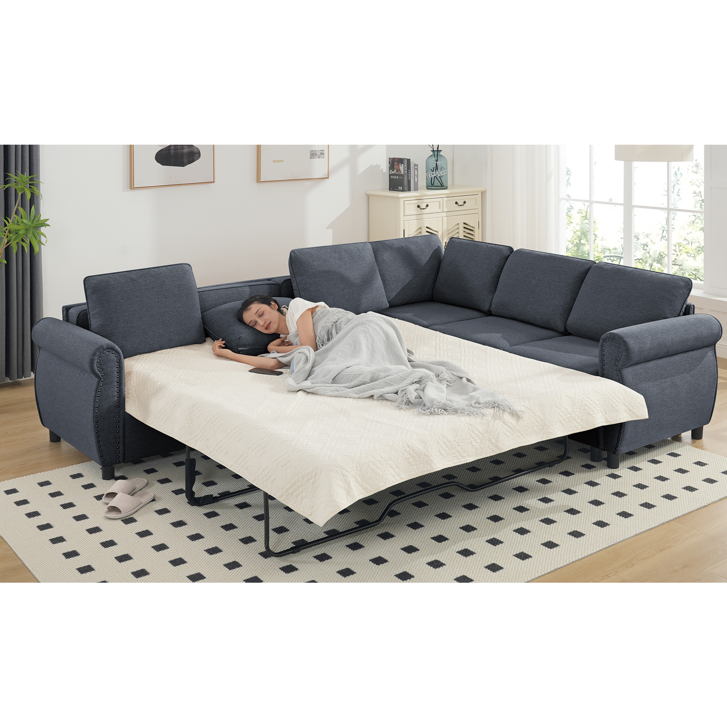 Dark gray fabric sectional sleeper sofa with nailhead trim and a woman sleeping on the extended mattress