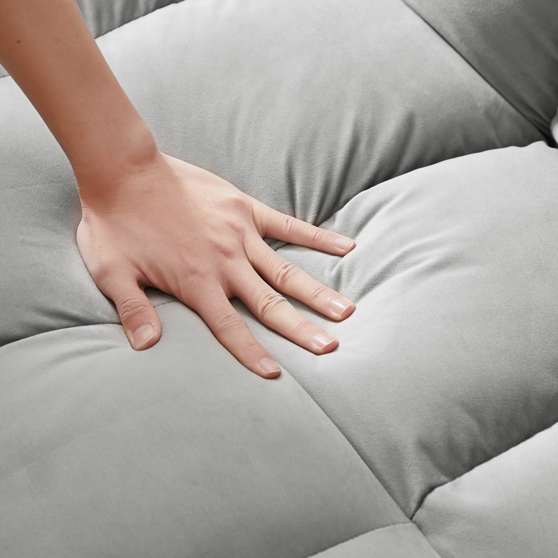 Hand pressing soft grey velvet sofa cushion with plush texture