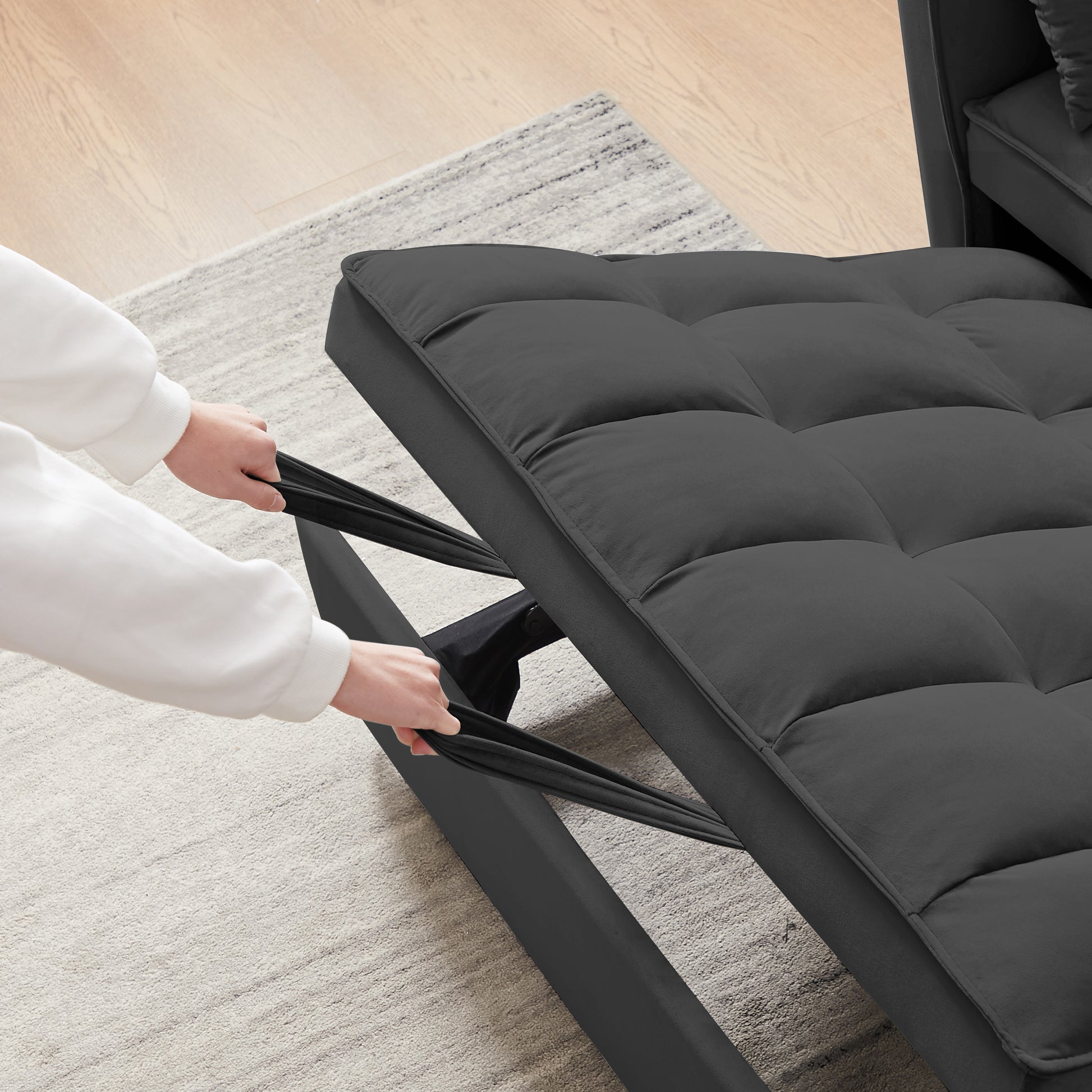 Dark gray upholstered sofa bed with tufted seat cushions being pulled open for conversion