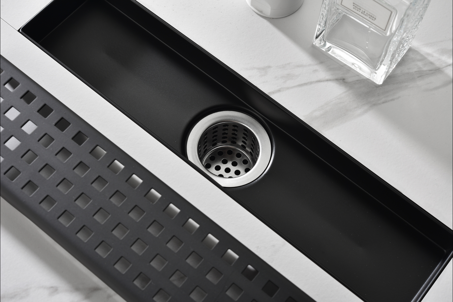 Sleek black linear drain with a perforated stainless steel strainer for a modern bathroom