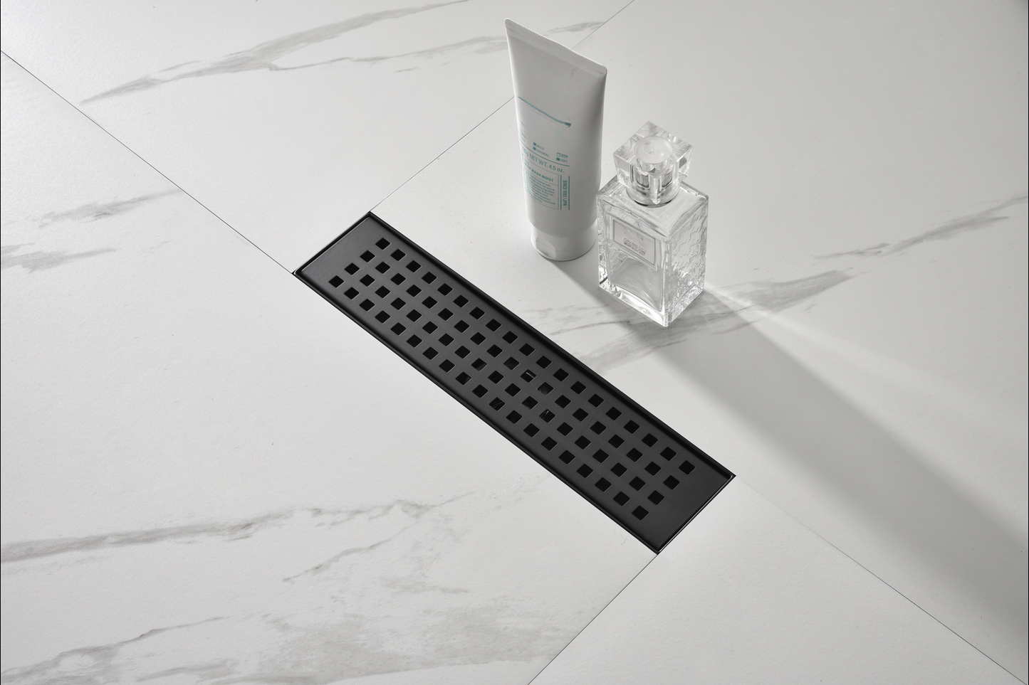 Black linear shower drain with a modern square pattern on a marblelook tile floor