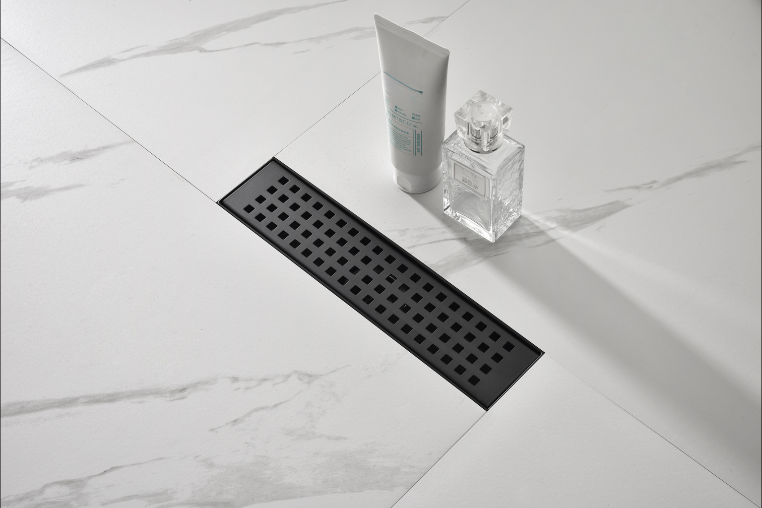Black linear shower drain with a modern square pattern on a marblelook tile floor